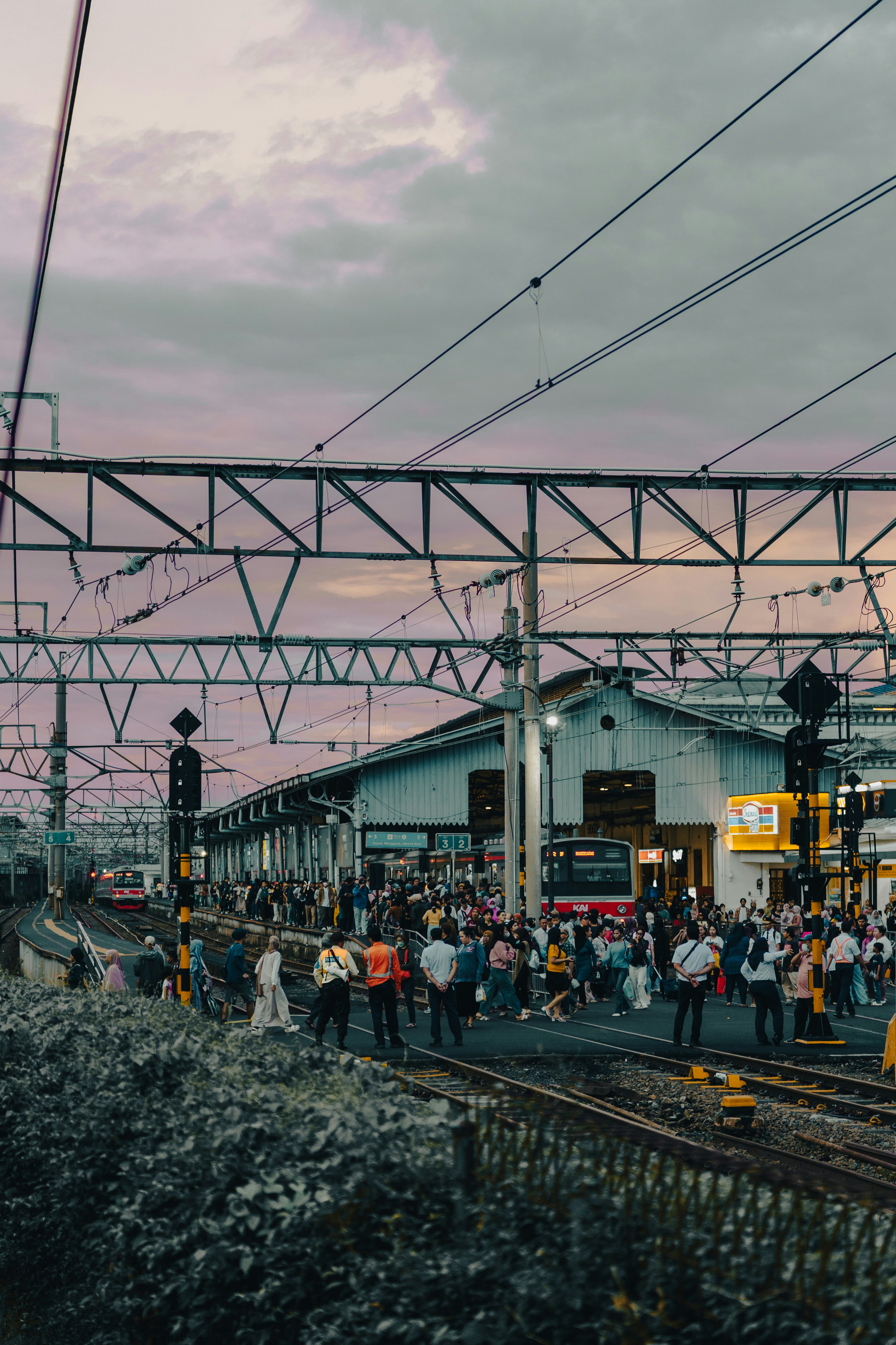 Quai de gare bondé au crépuscule avec des fils aériens