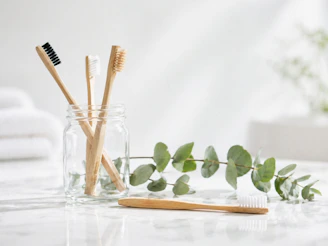Bamboo toothbrushes in a glass jar with eucalyptus leaves.