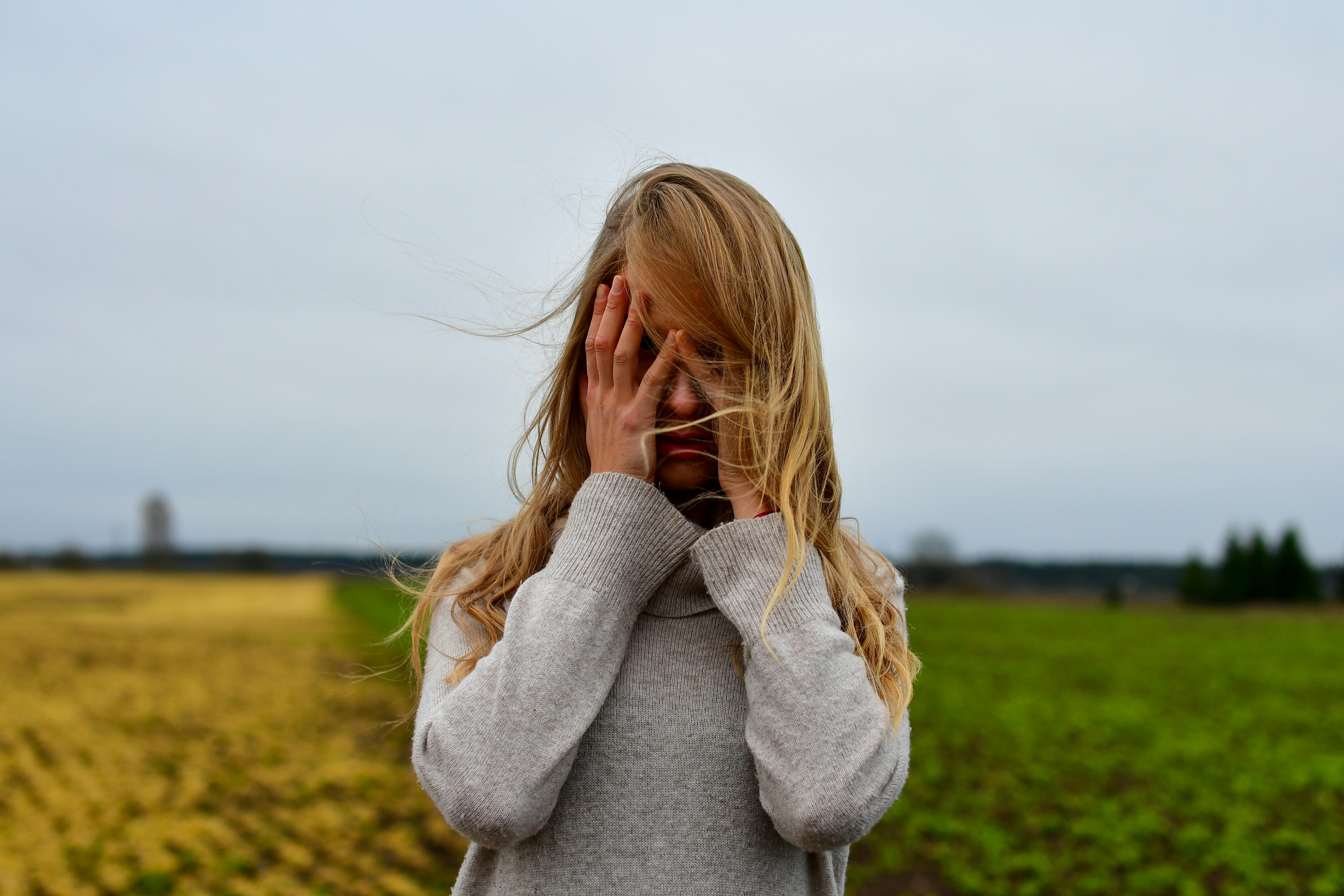 Young girl covers face with hands in field.
