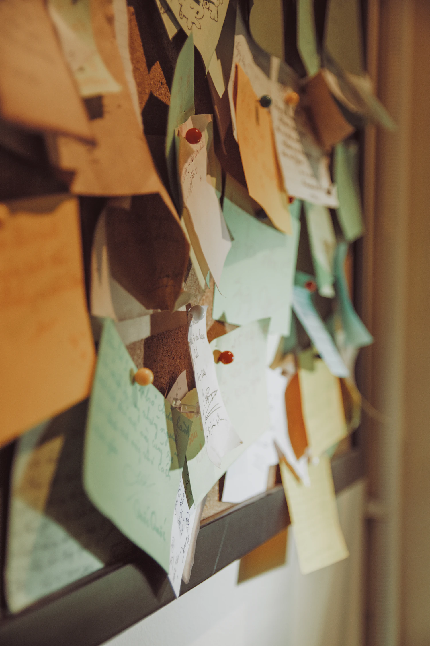 Overlapping handwritten slips in soft greens and browns held to a board with round-headed pins