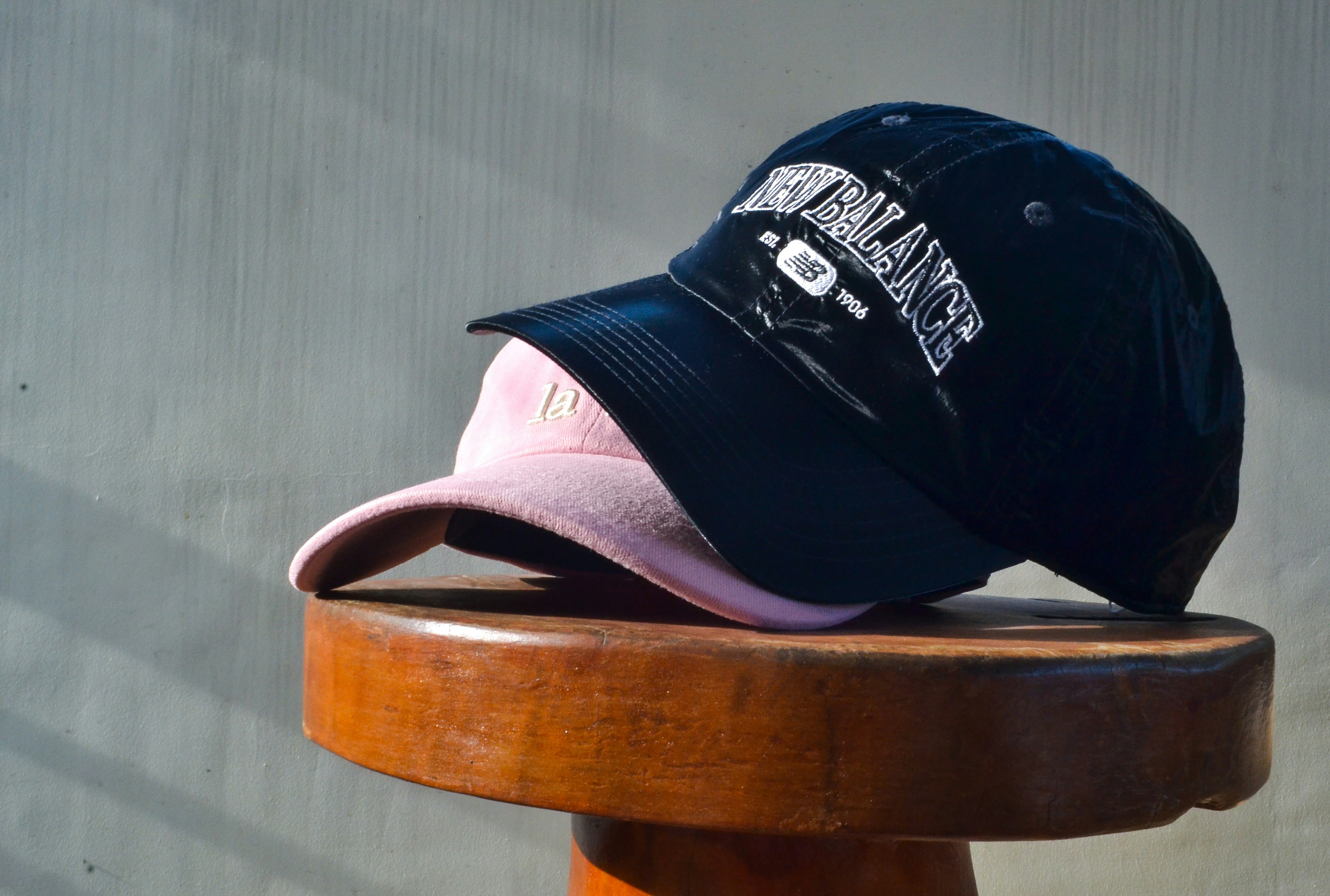 Two baseball caps on a wooden stool.