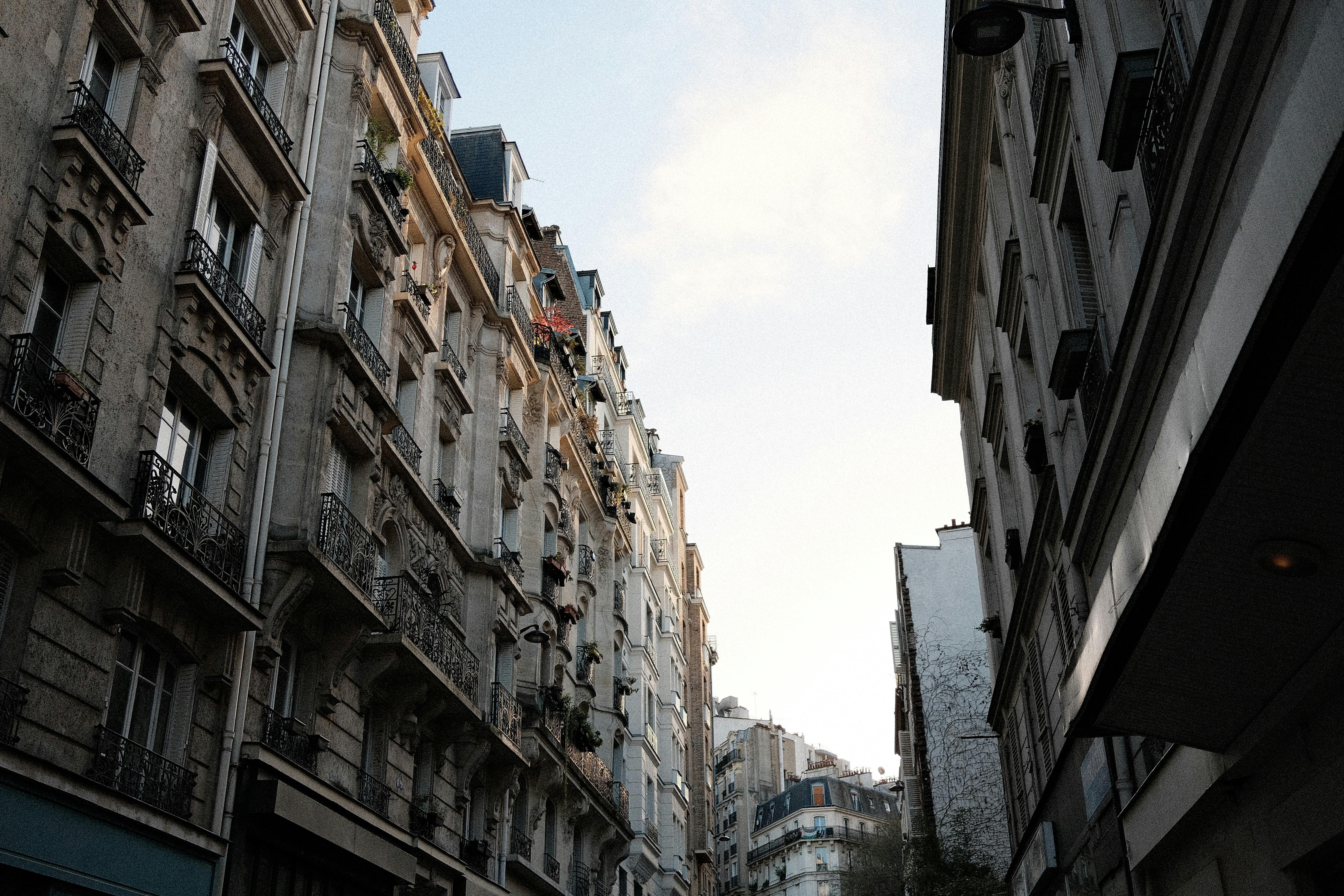 De hauts immeubles bordent une rue étroite sous un ciel lumineux.
