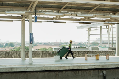 Man in hard hat pulls large green suitcase on platform.