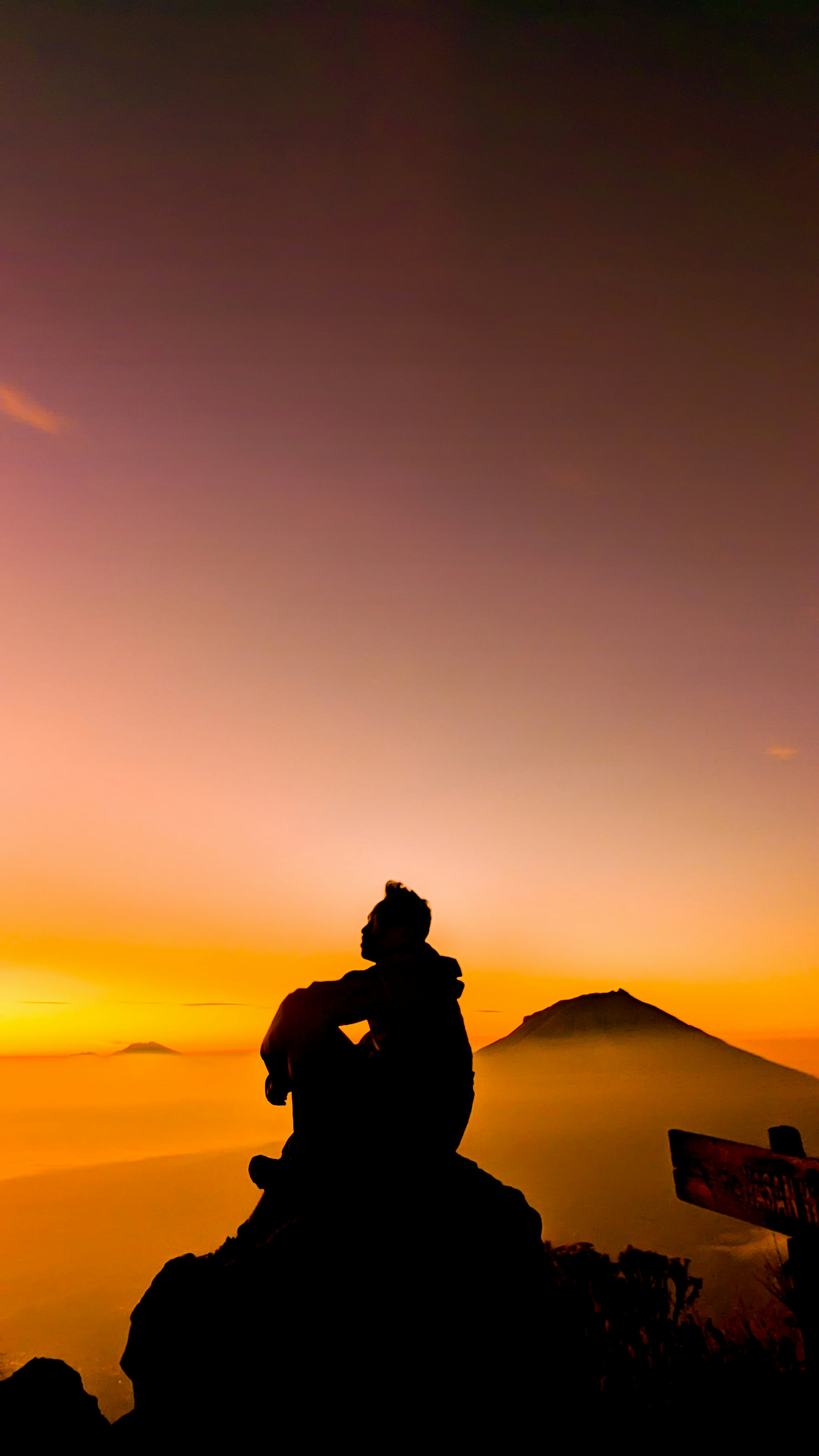 Silhouette of a person sitting on a mountain at sunset