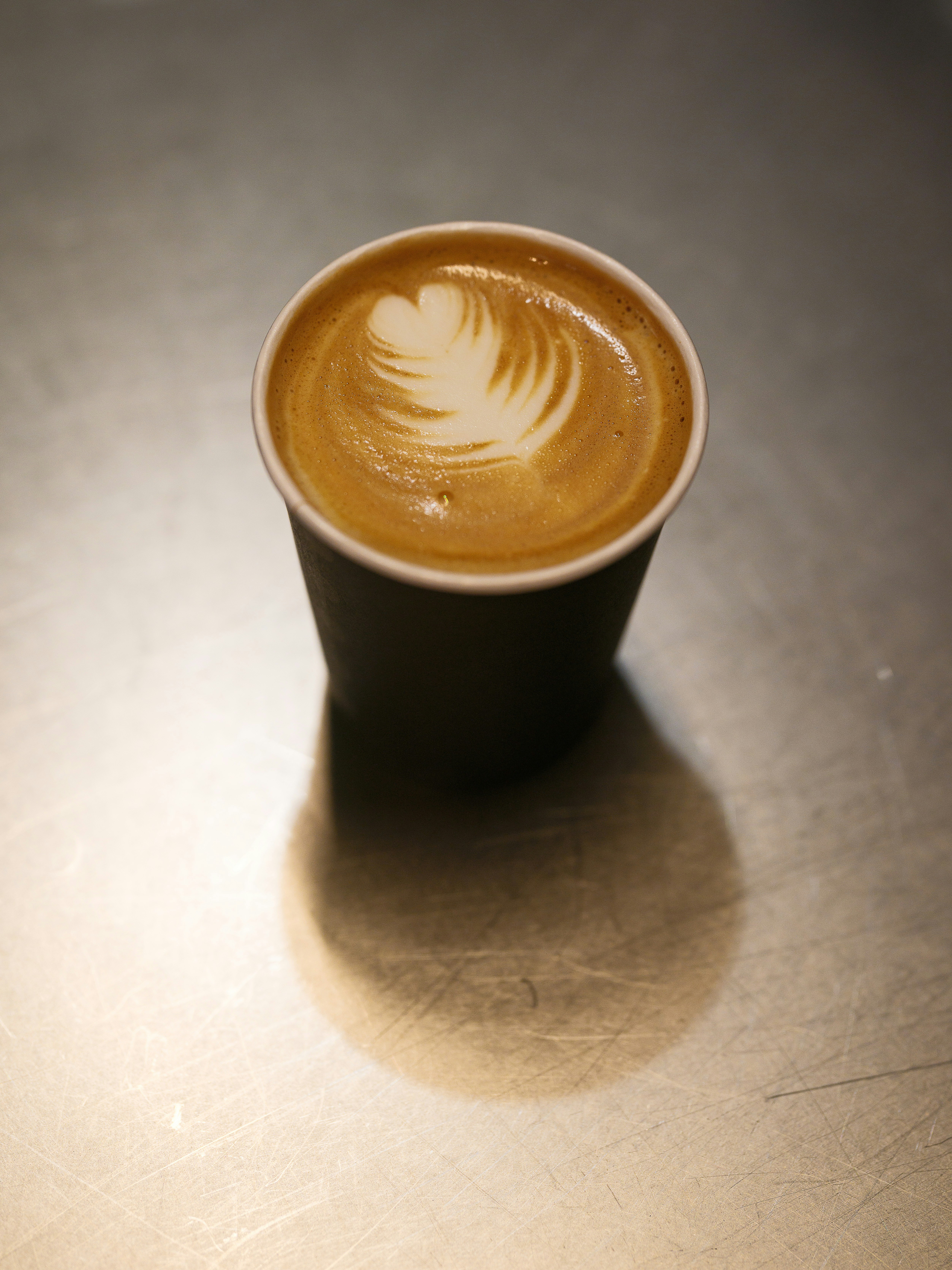 Latte Art in einem To-Go-Becher auf einer Metalloberfläche