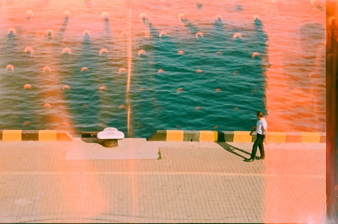 man-walks-along-a-sunny-waterfront-with-teal-water-1CVyZNSDzic.png