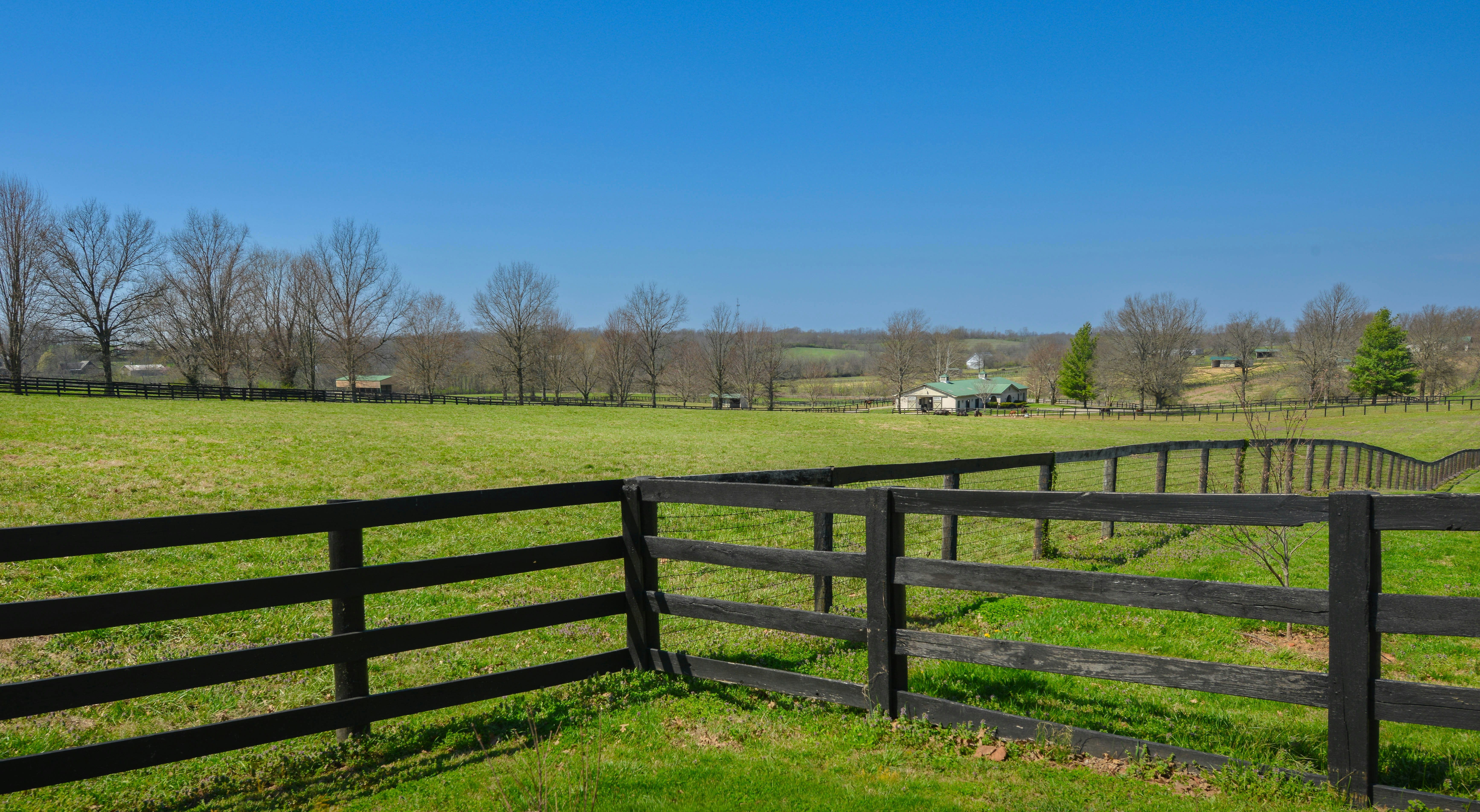 A wooden fence borders a green pasture with a barn.