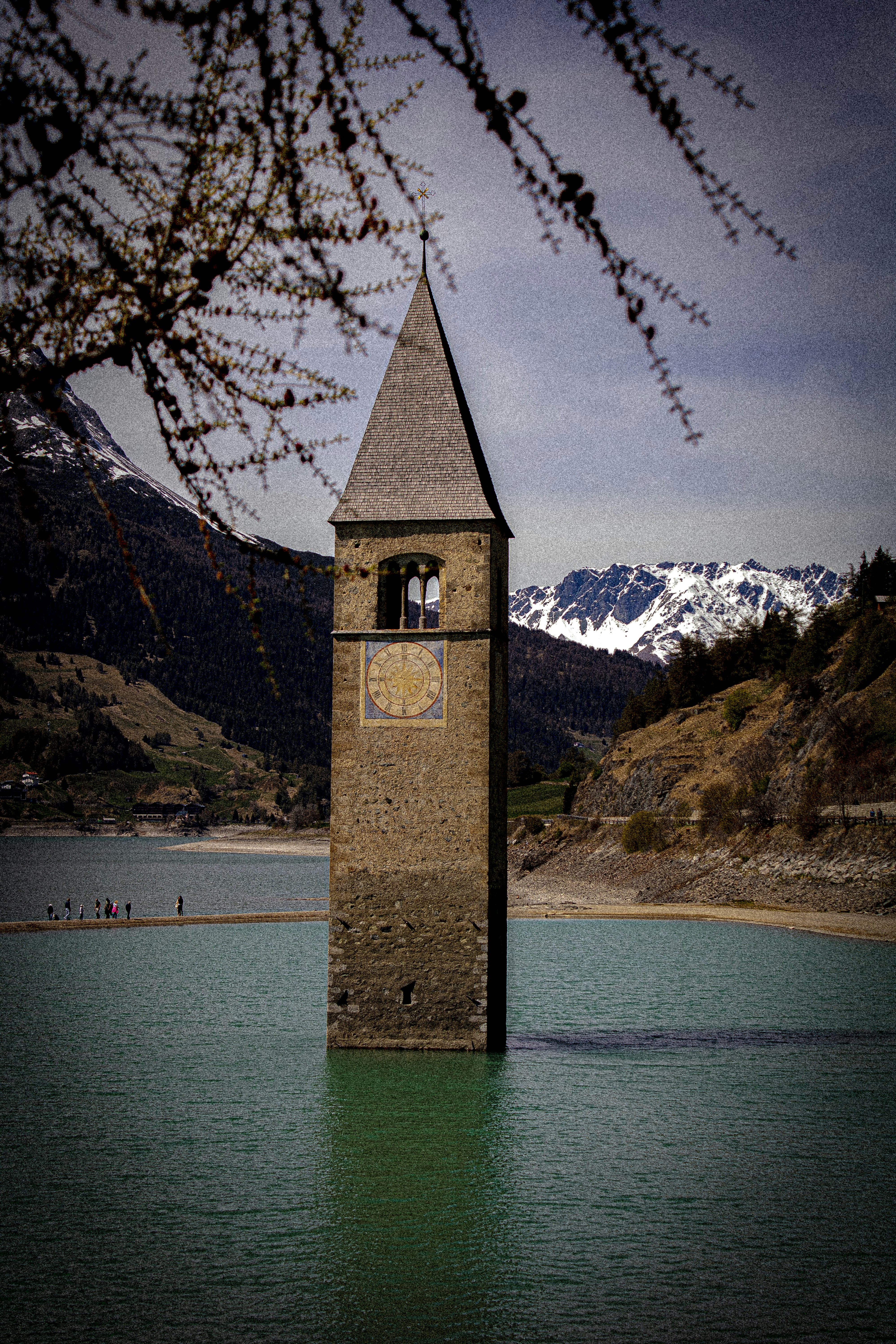 Menara lonceng muncul dari danau yang tenang dengan pegunungan.