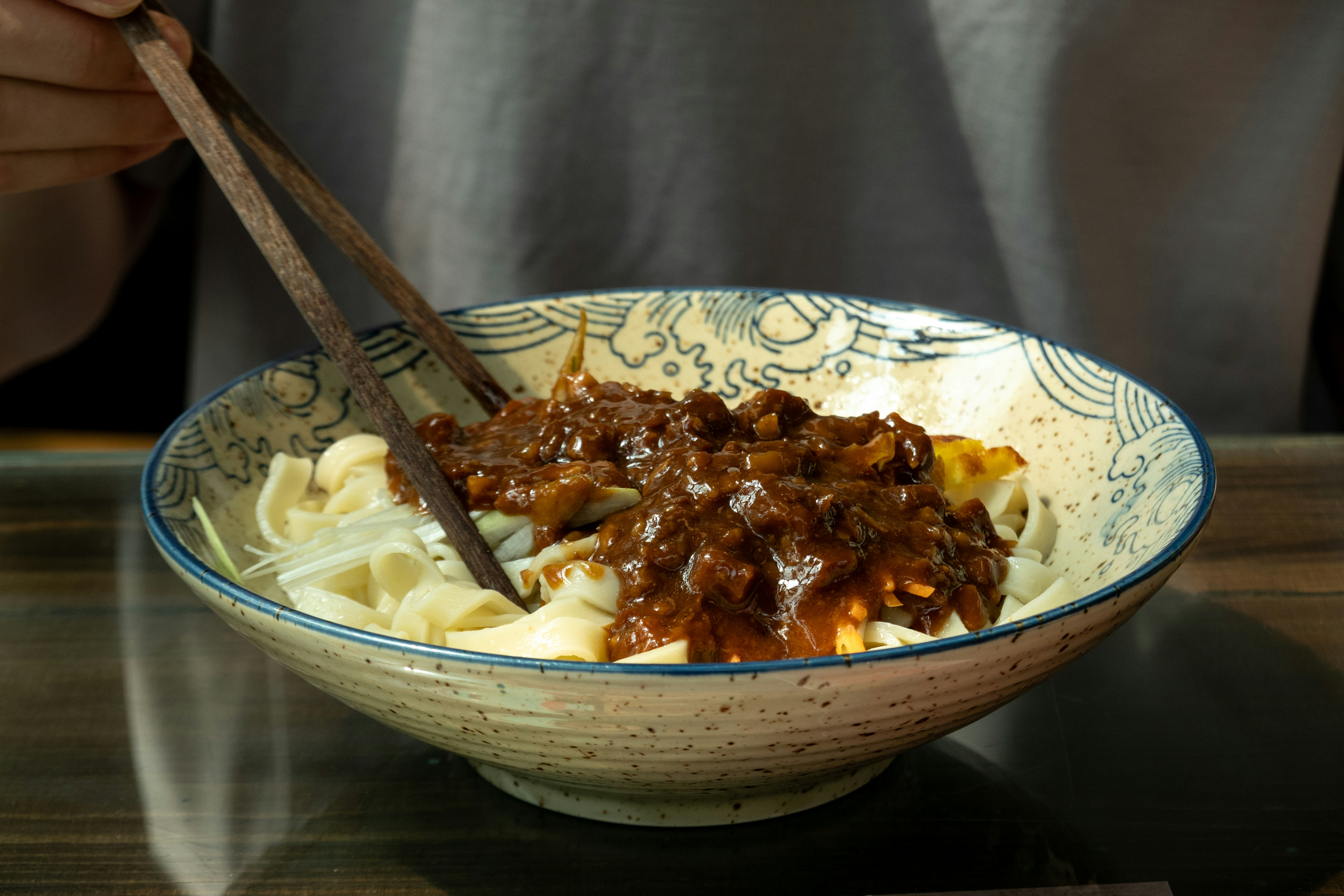 Person eating noodles with chopsticks from a decorative bowl