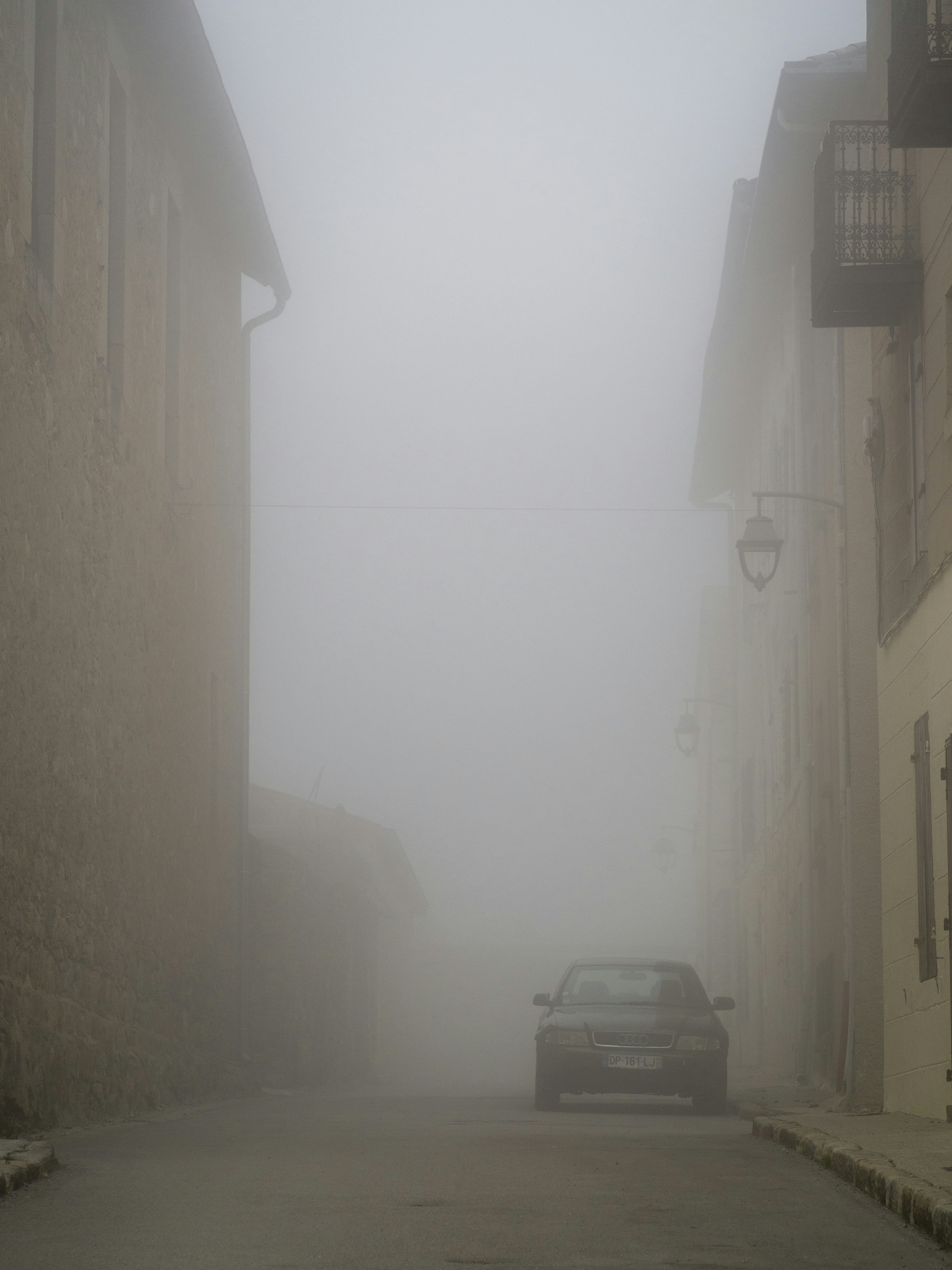 A car parked on a foggy street between buildings.