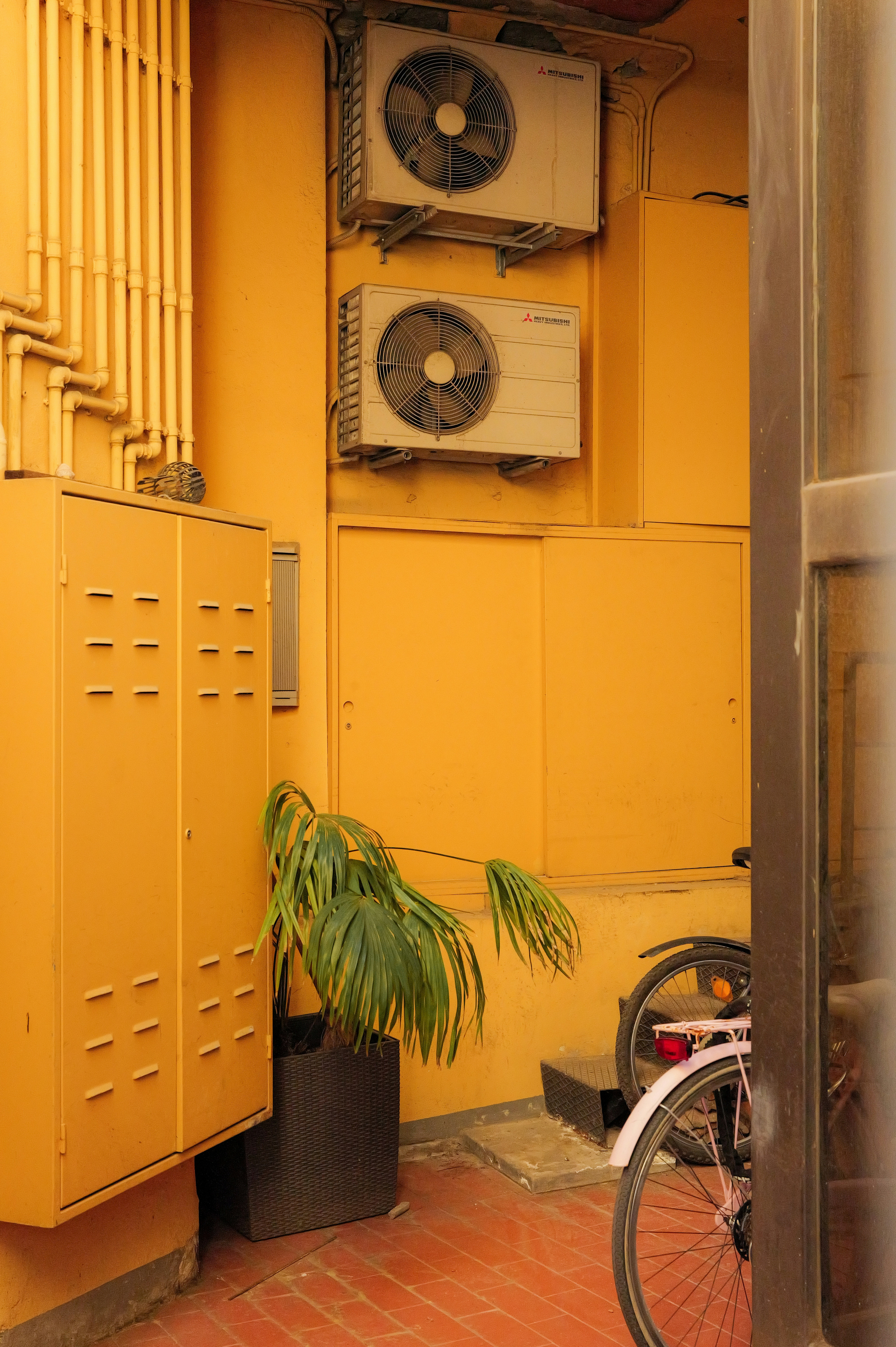 Two air conditioning units on a yellow wall.