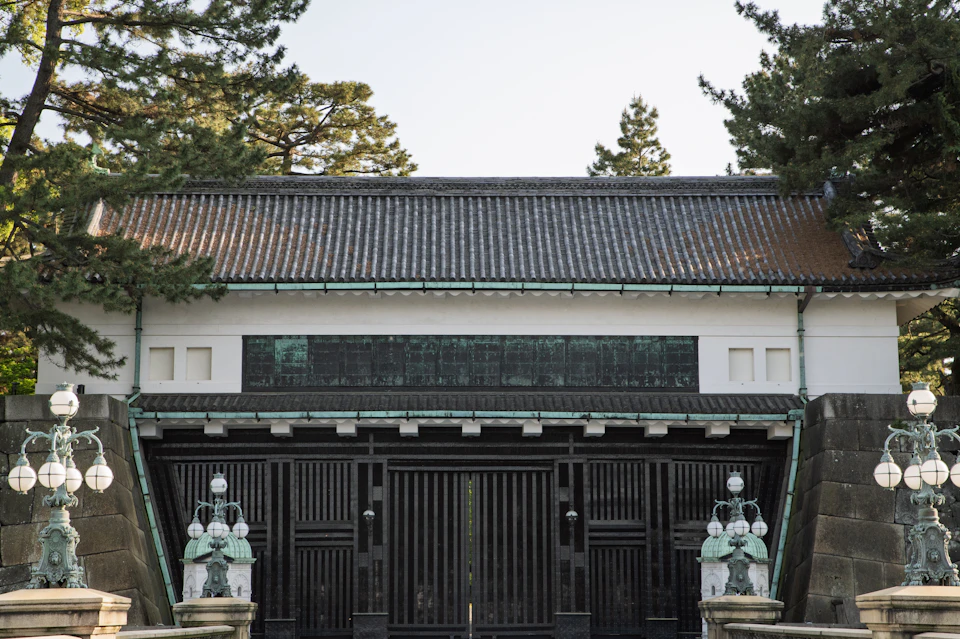 The image depicts a traditional Japanese temple with a white facade and black roof, situated amidst lush greenery. The temple is surrounded by trees, creating a serene atmosphere. Two large stone gates are prominently displayed at the entrance to the temple, each adorned with intricate carvings of animals and plants. These gateways serve as a symbol of protection and spiritual guidance for those entering the temple grounds.