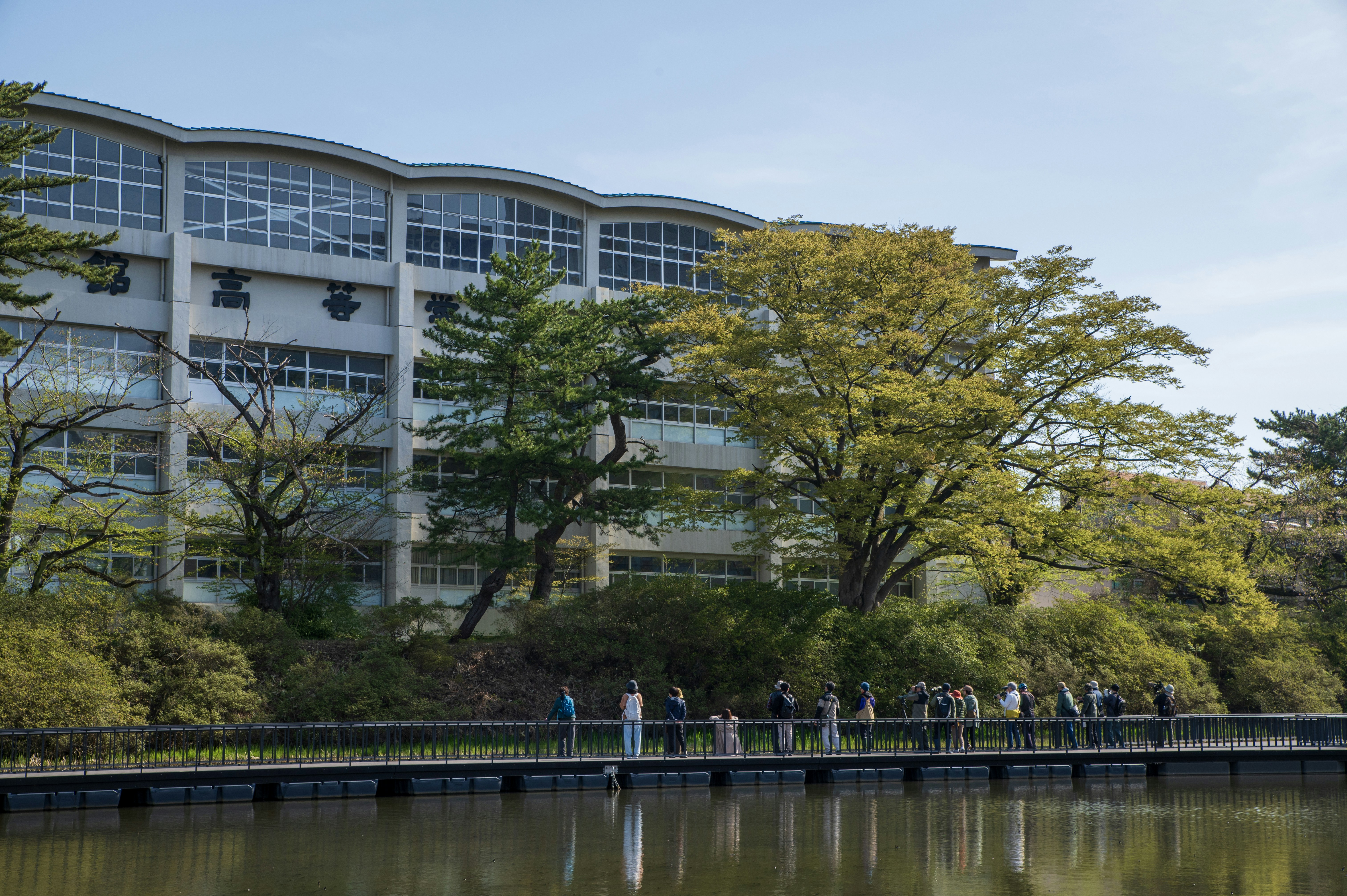 Modern building beside a tranquil lake with people walking.
