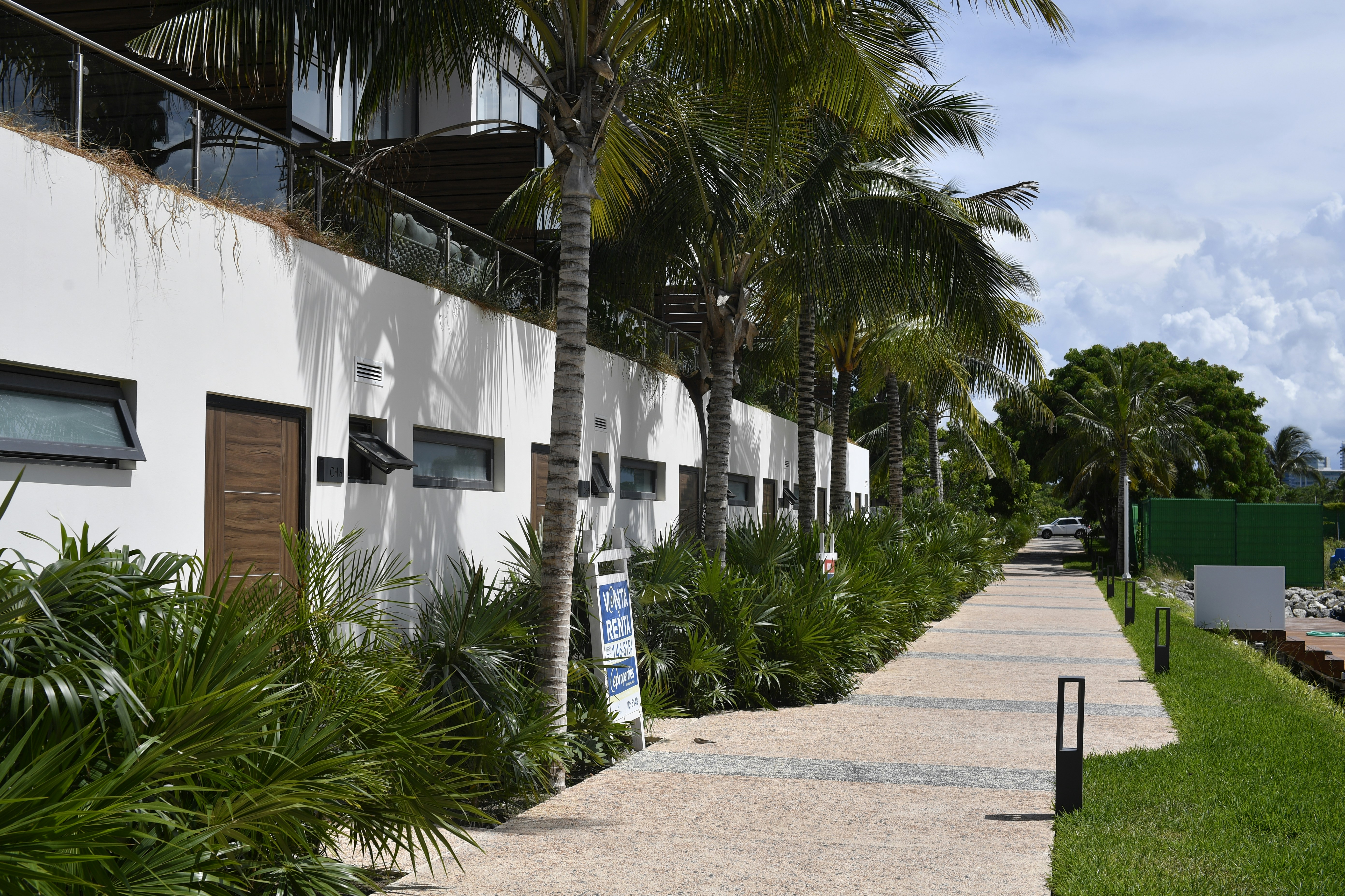 Modern white tropical villas with palm trees and a scenic pedestrian walkway under a bright sky.