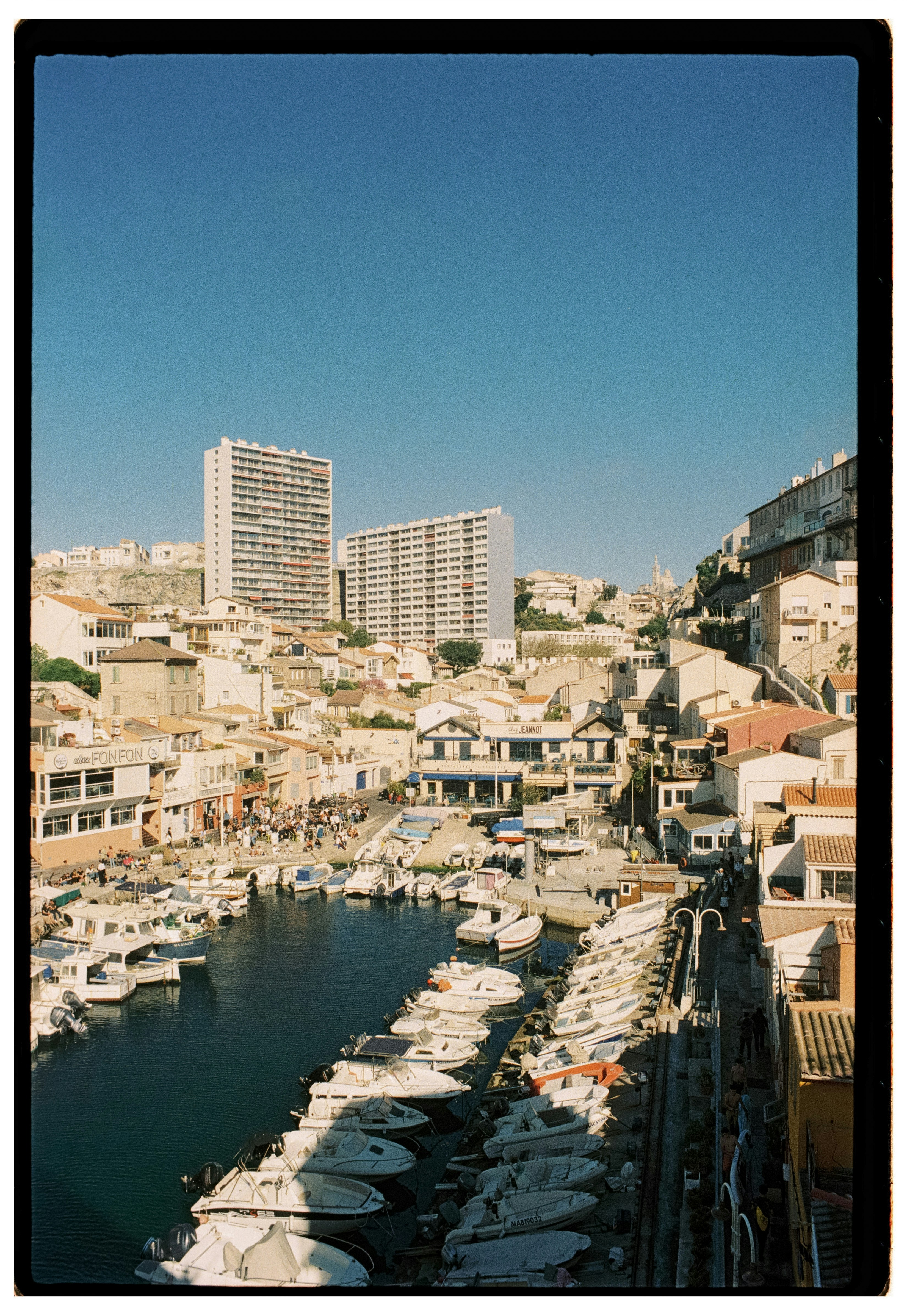 Des bateaux accostés dans un port ensoleillé avec des bâtiments et des collines.