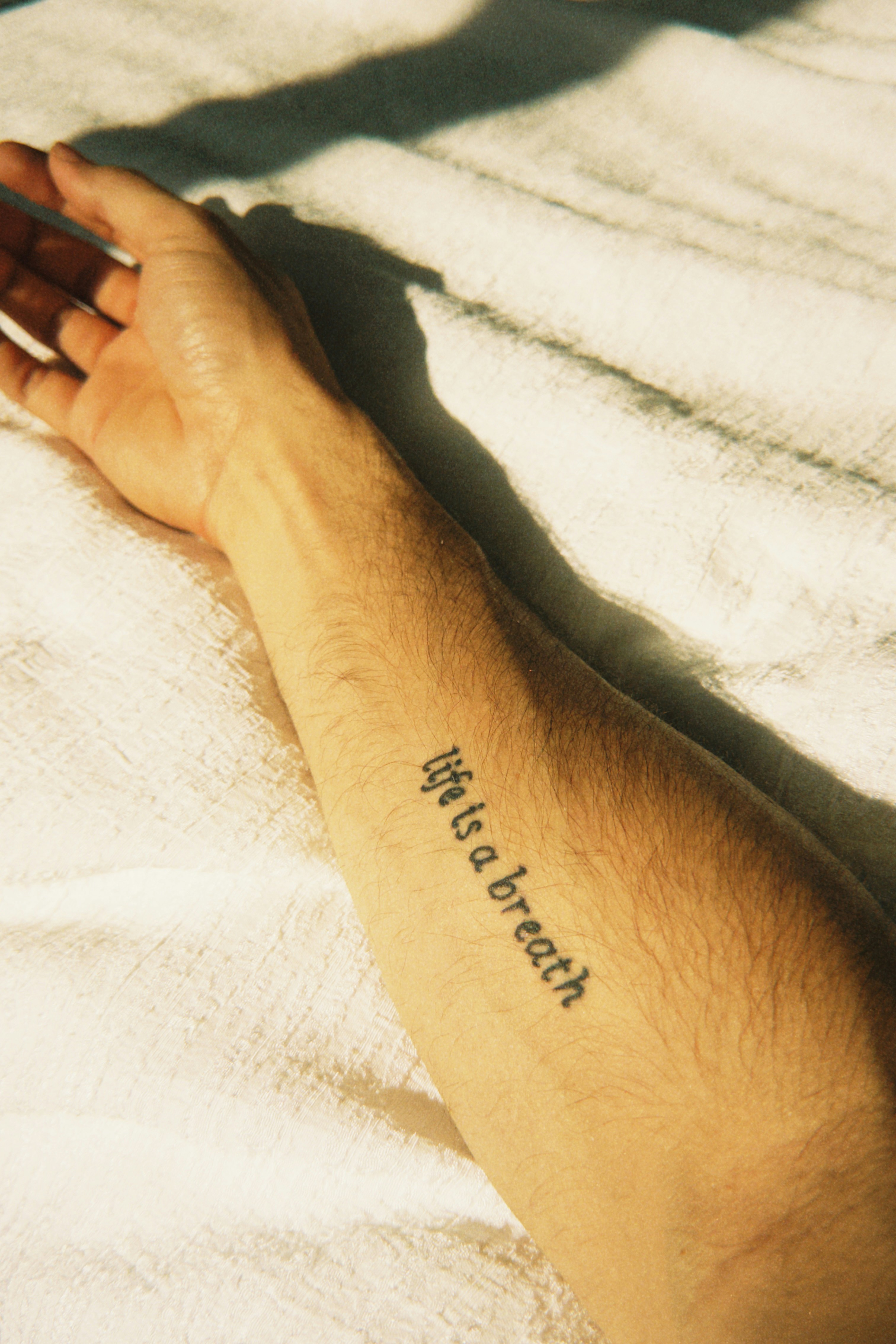 A tattoo on an arm reads 'life is a breath'.