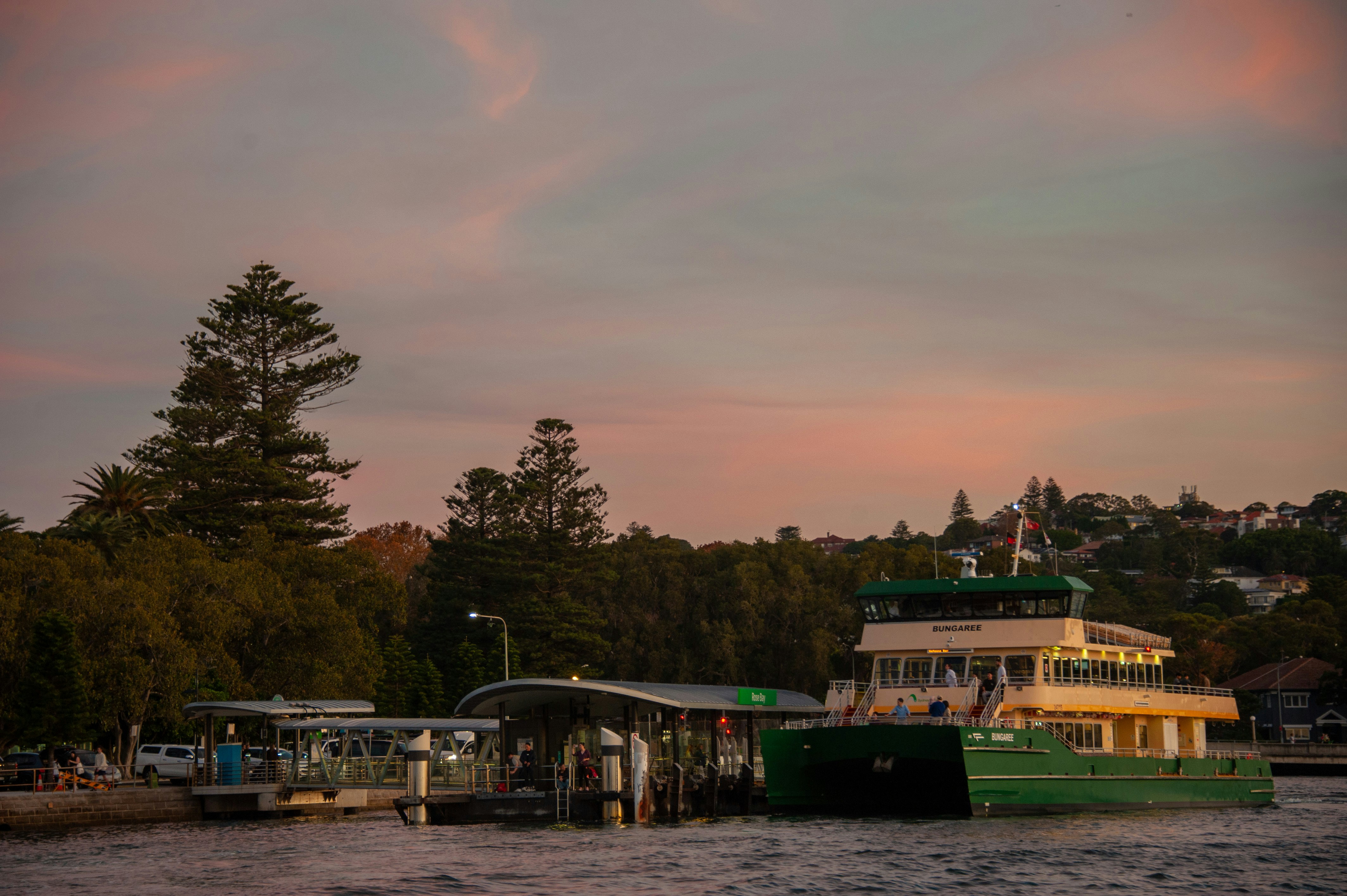 A green ferry docked at a pier during sunset.
