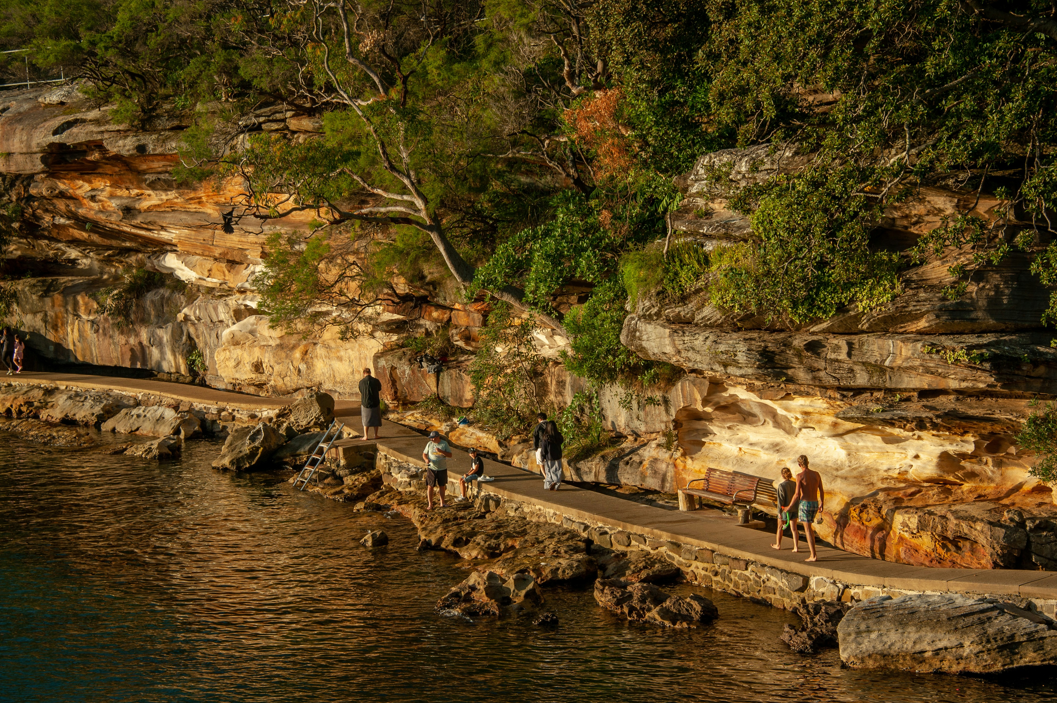 People walking along a scenic coastal path beside rocky cliffs.
