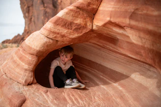 Boy sitting in a sandstone cave with striped rock formations.
