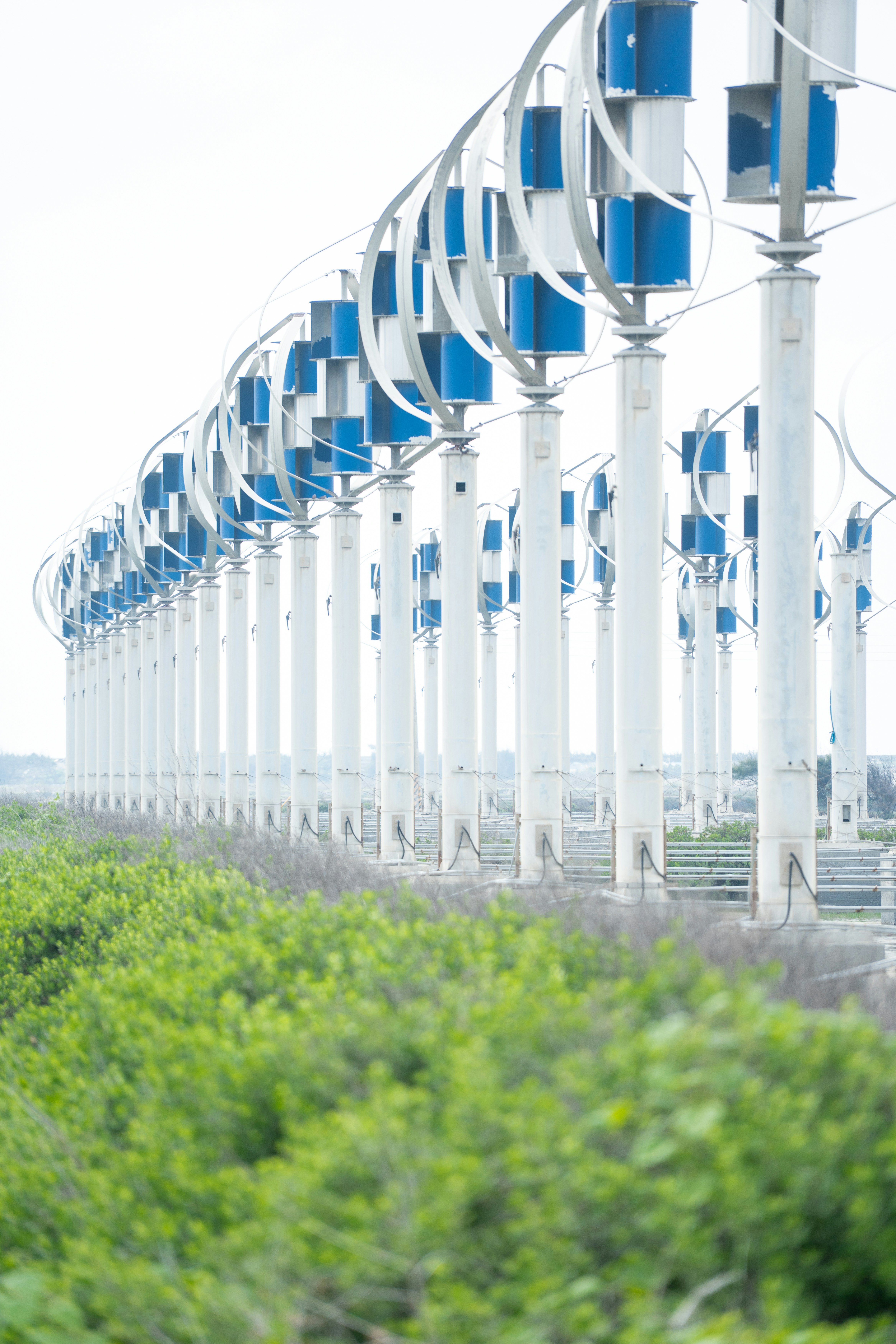 A row of vertical axis wind turbines in a field.