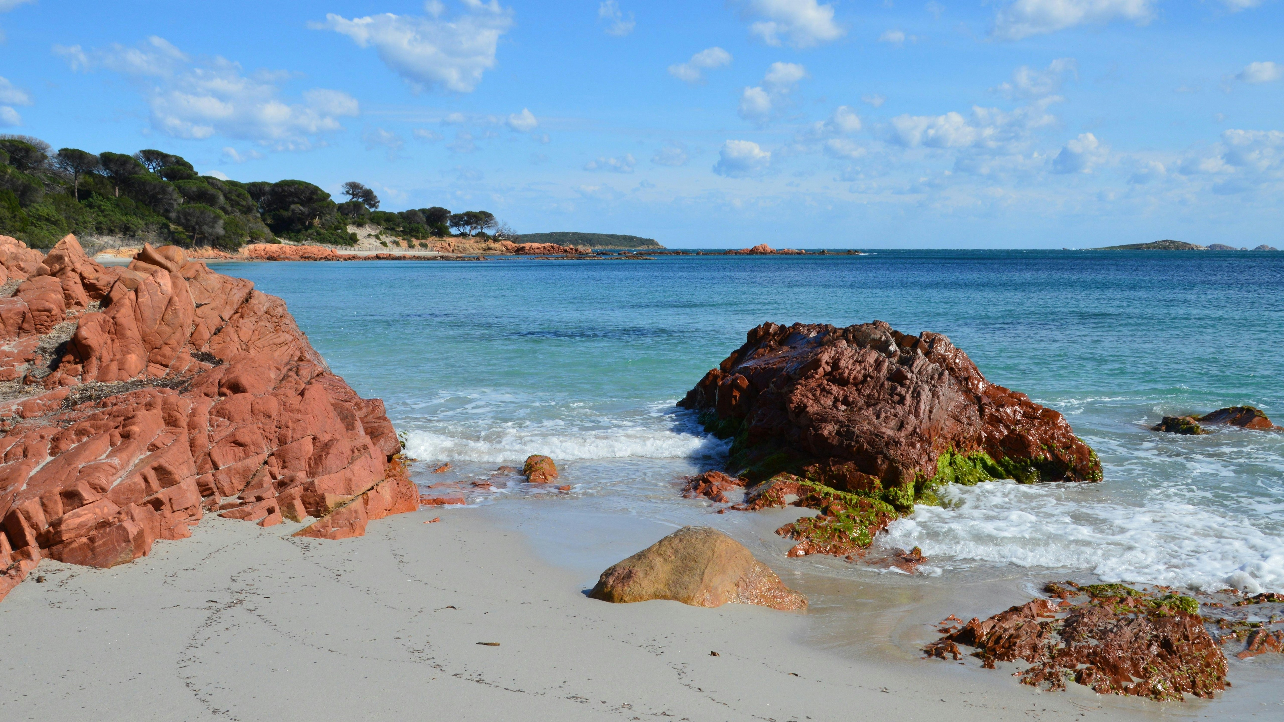 Red rocks and sandy beach meet the blue ocean