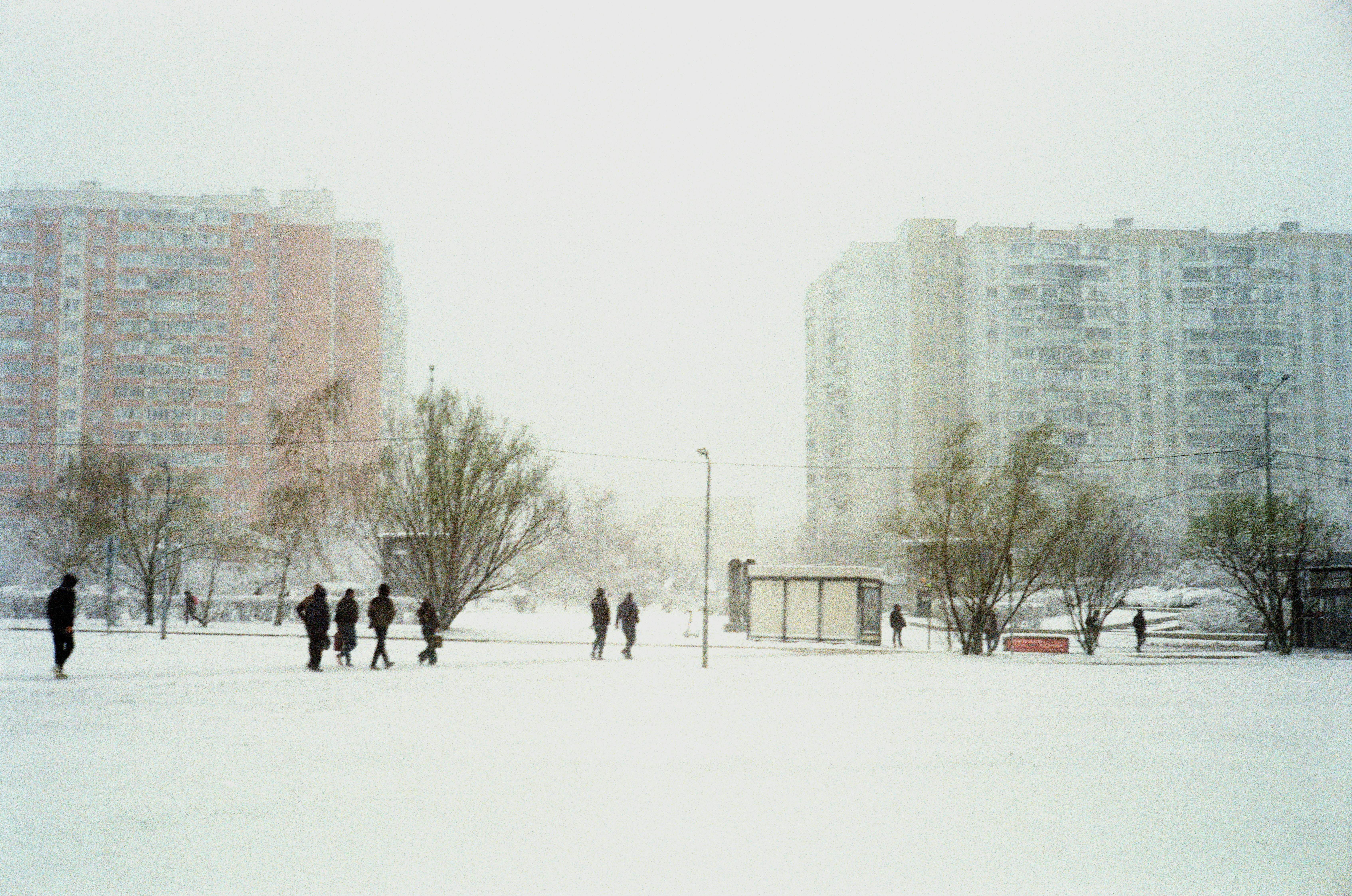 Pessoas caminhando em um parque nevado entre prédios de apartamentos.