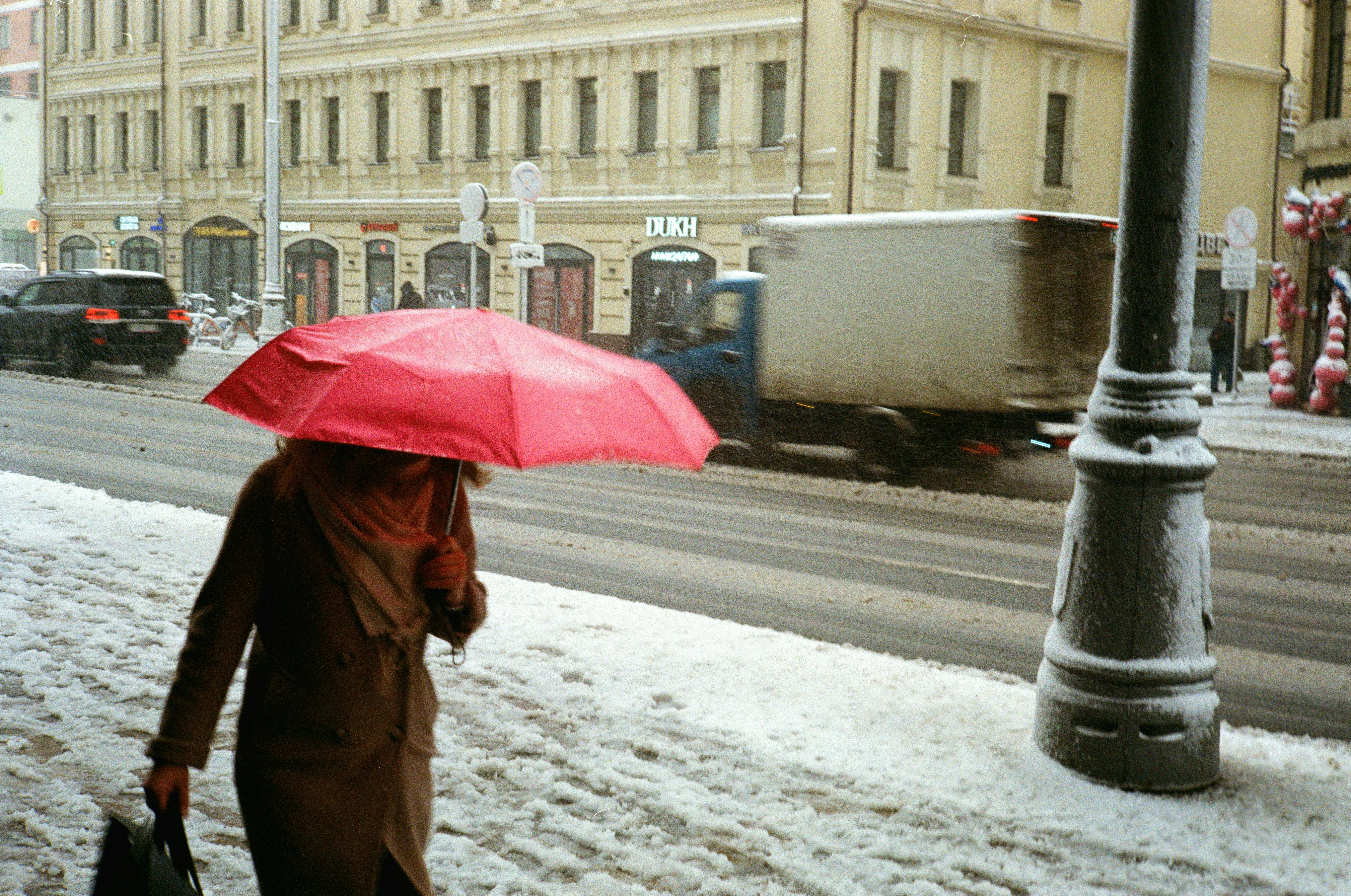 Mulher segurando guarda-chuva vermelho andando na calçada nevada