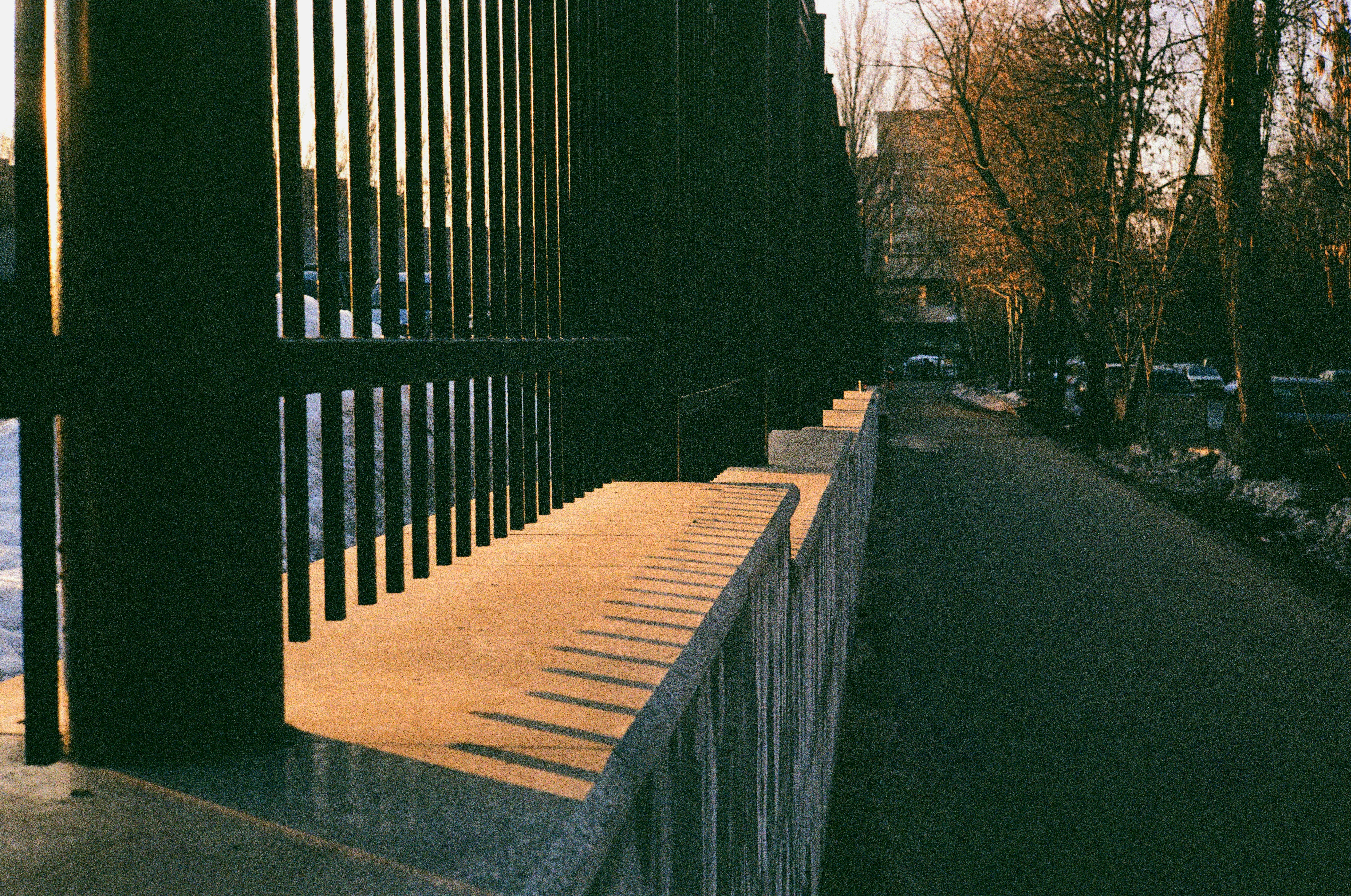 Um corrimão de concreto iluminado pelo sol ao lado de uma cerca de metal escuro.
