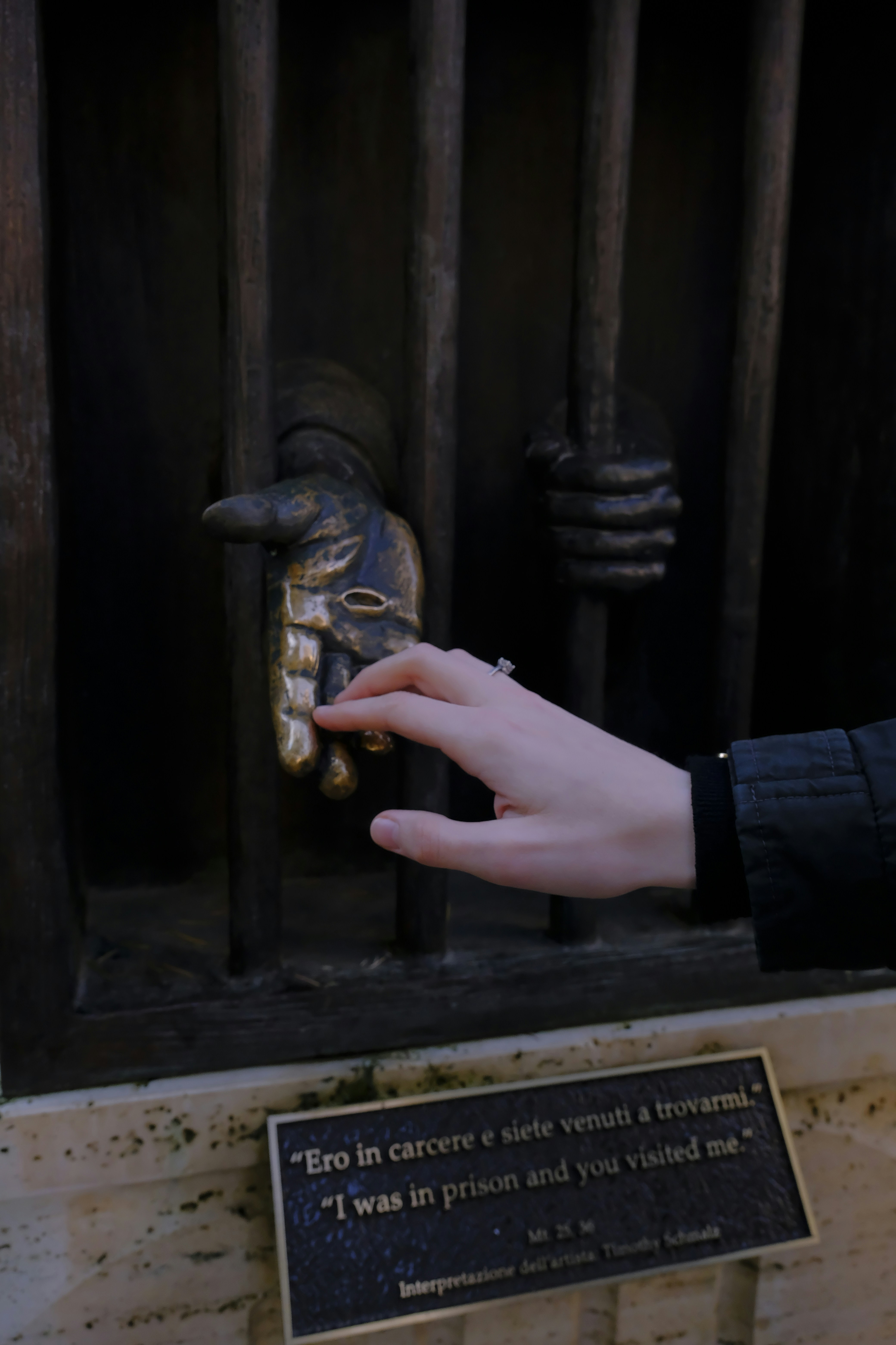 A hand reaches through prison bars toward a plaque.