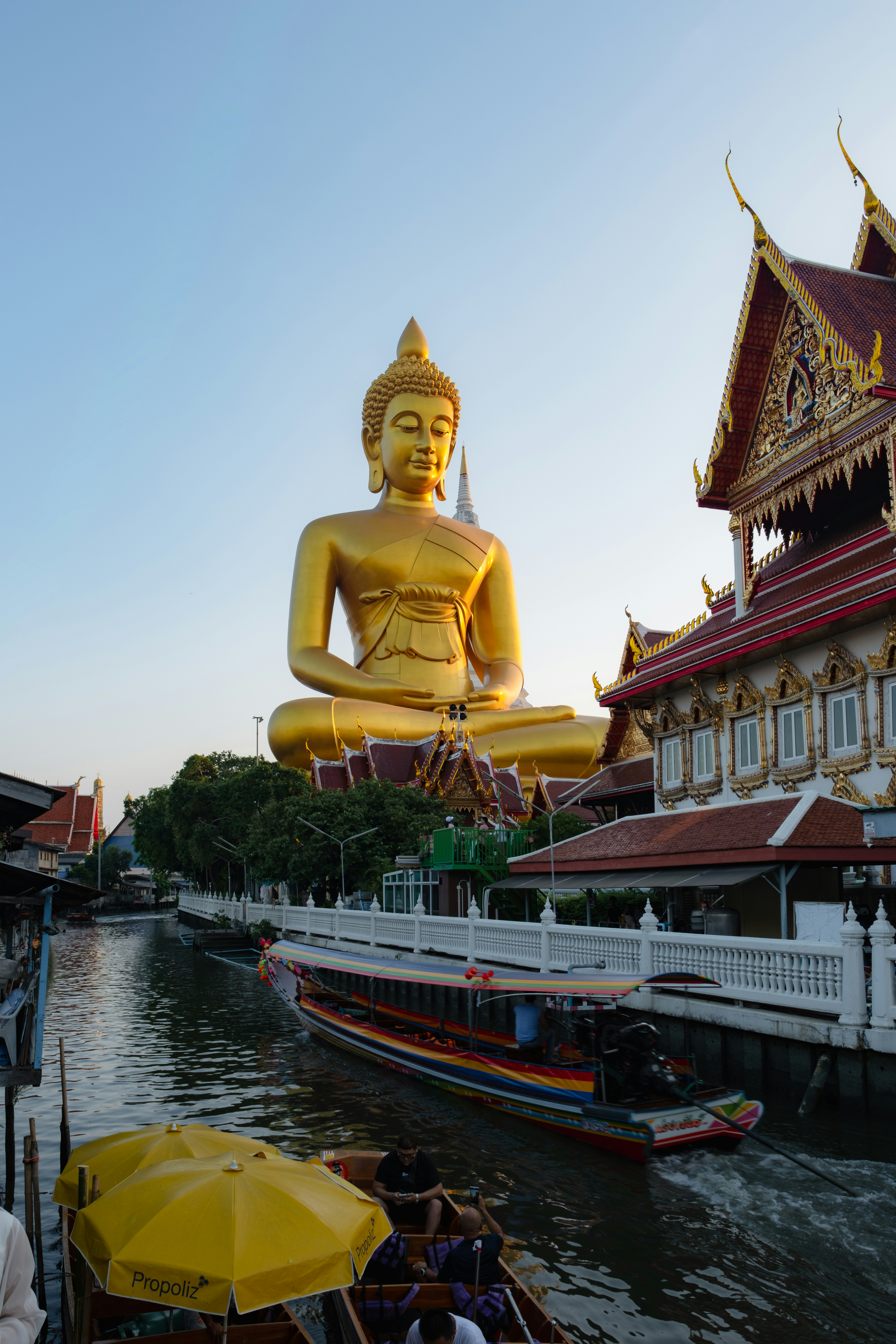 Giant golden buddha statue overlooking a canal with boats.
