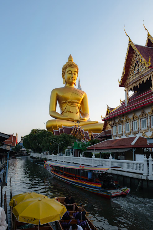 Giant golden buddha statue overlooking a canal with boats