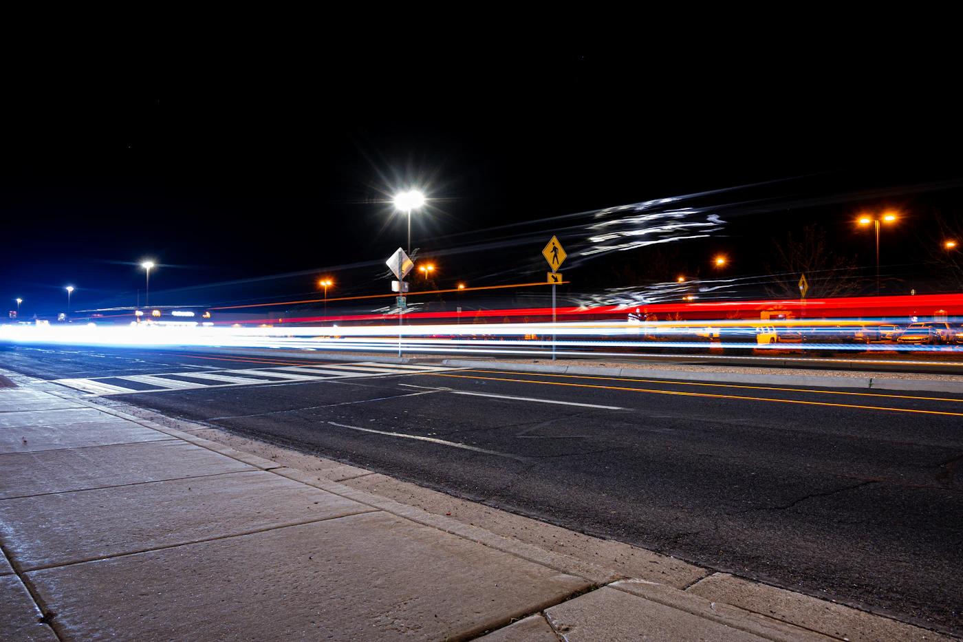 Rua da cidade à noite com rastros de luz de carros em movimento