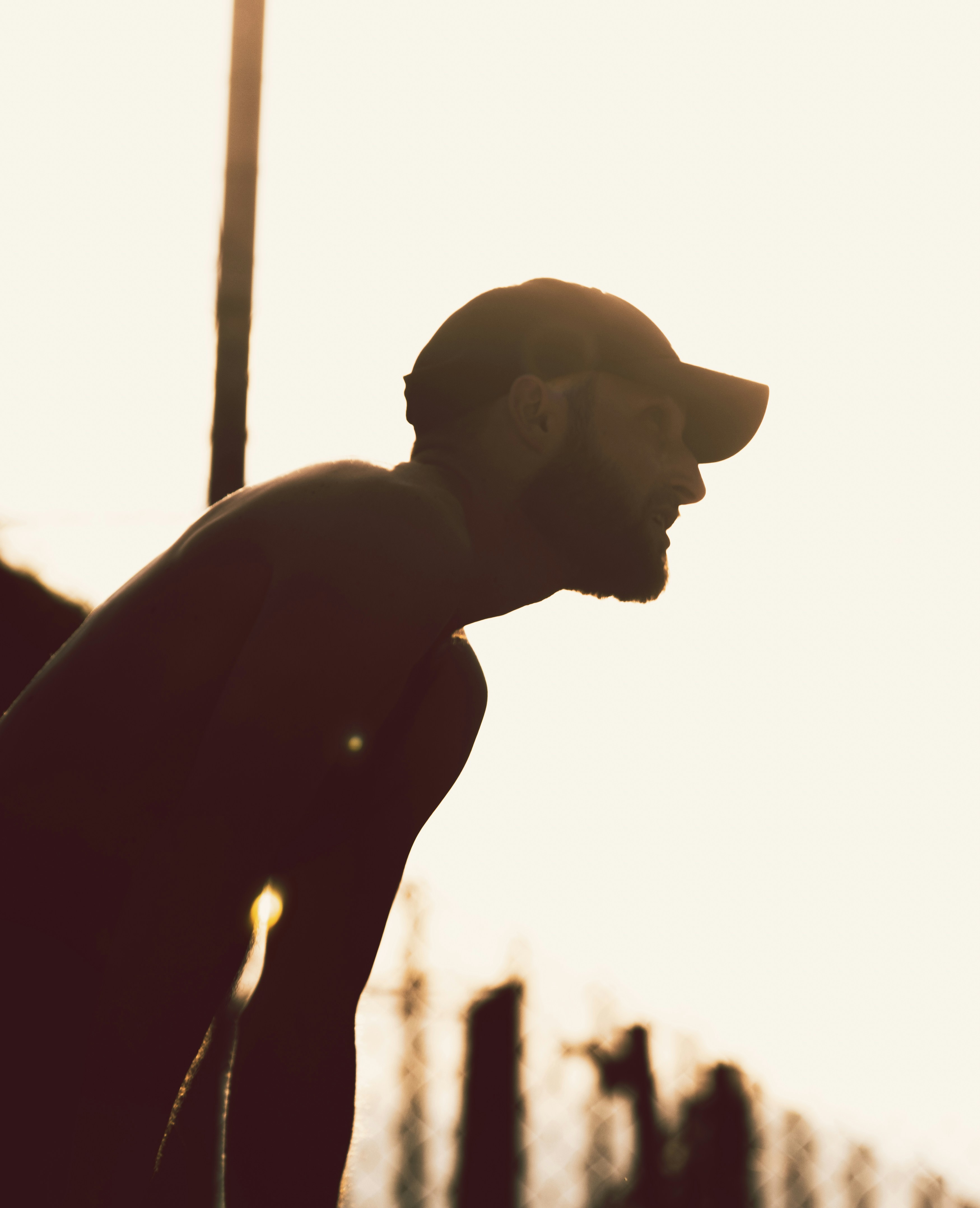 Silhouette of a man wearing a baseball cap outdoors.