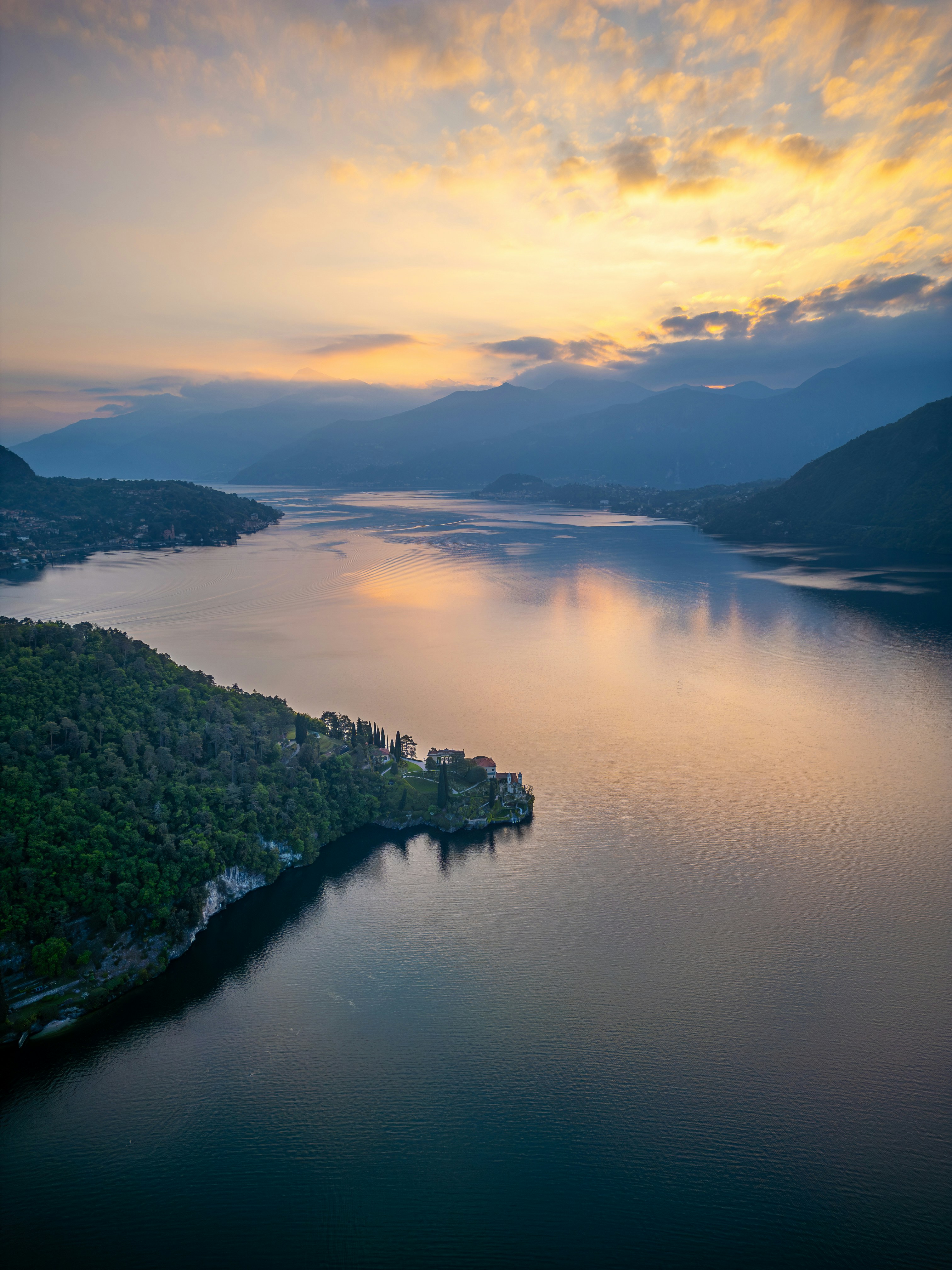 Serene lake and mountains at sunrise with soft clouds.