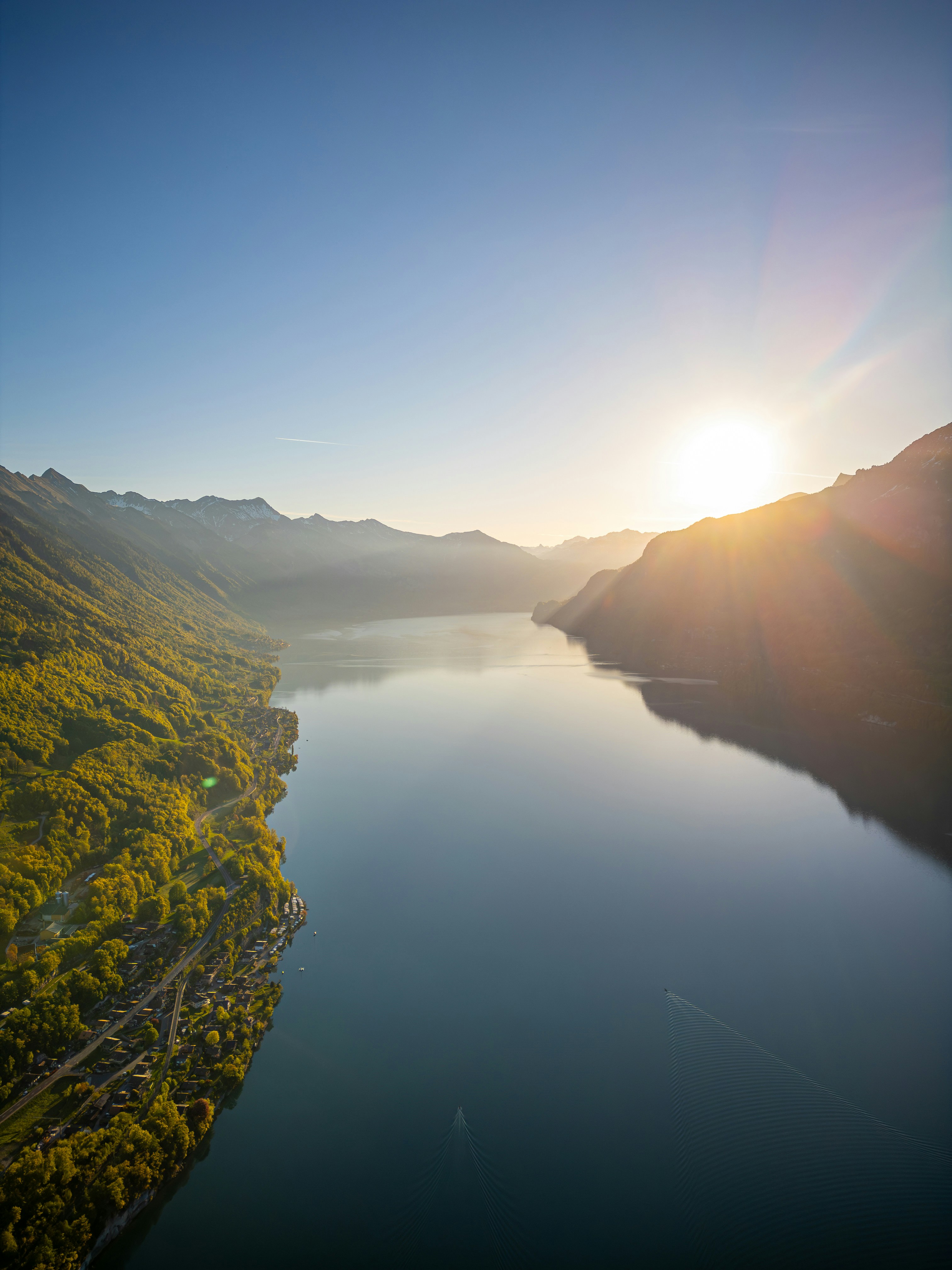 Sunrise over a tranquil lake with forested mountains.