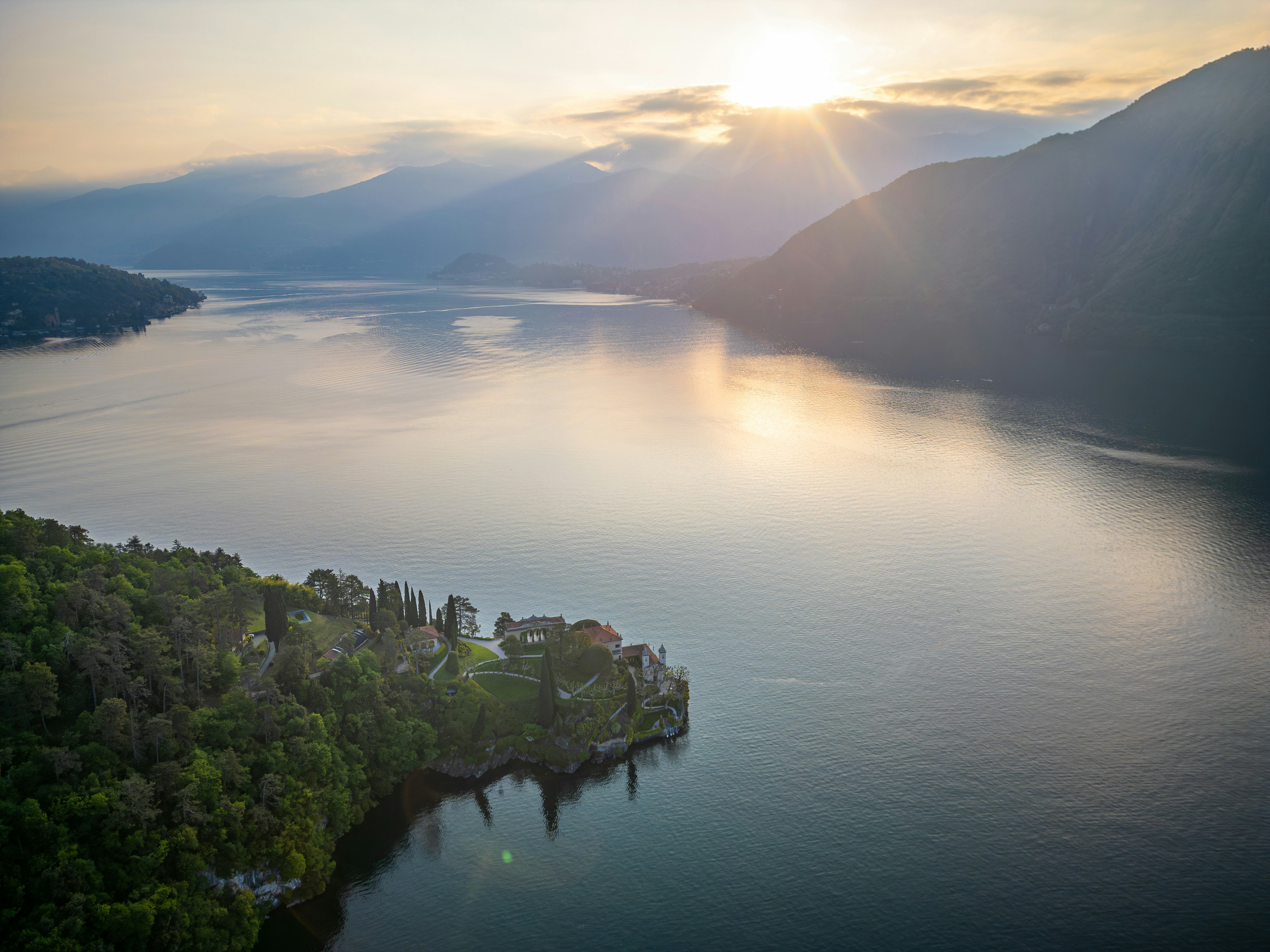Sunbeams over a serene lake and forested peninsula.