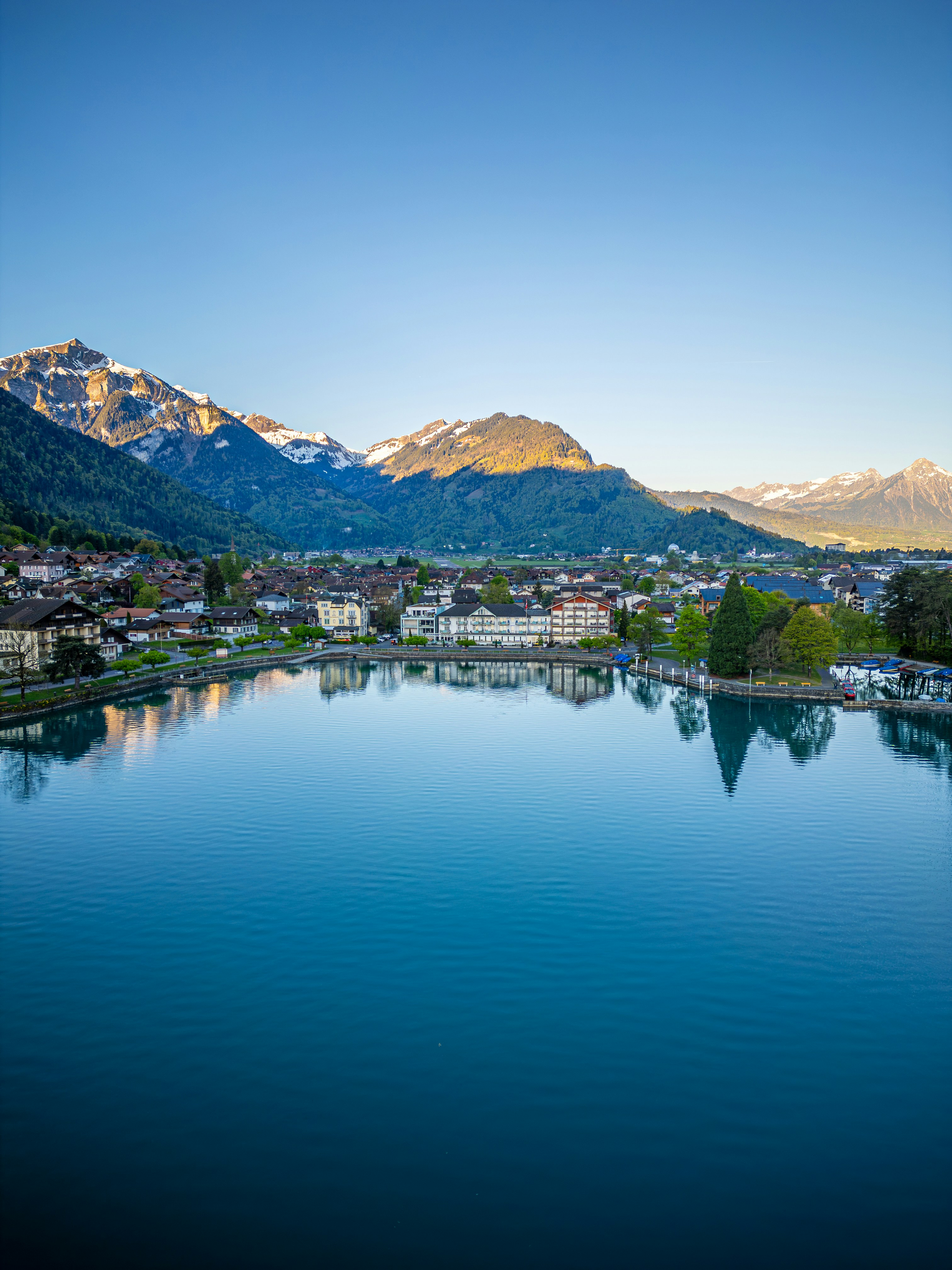 Calm lake reflects town nestled below snow-capped mountains.
