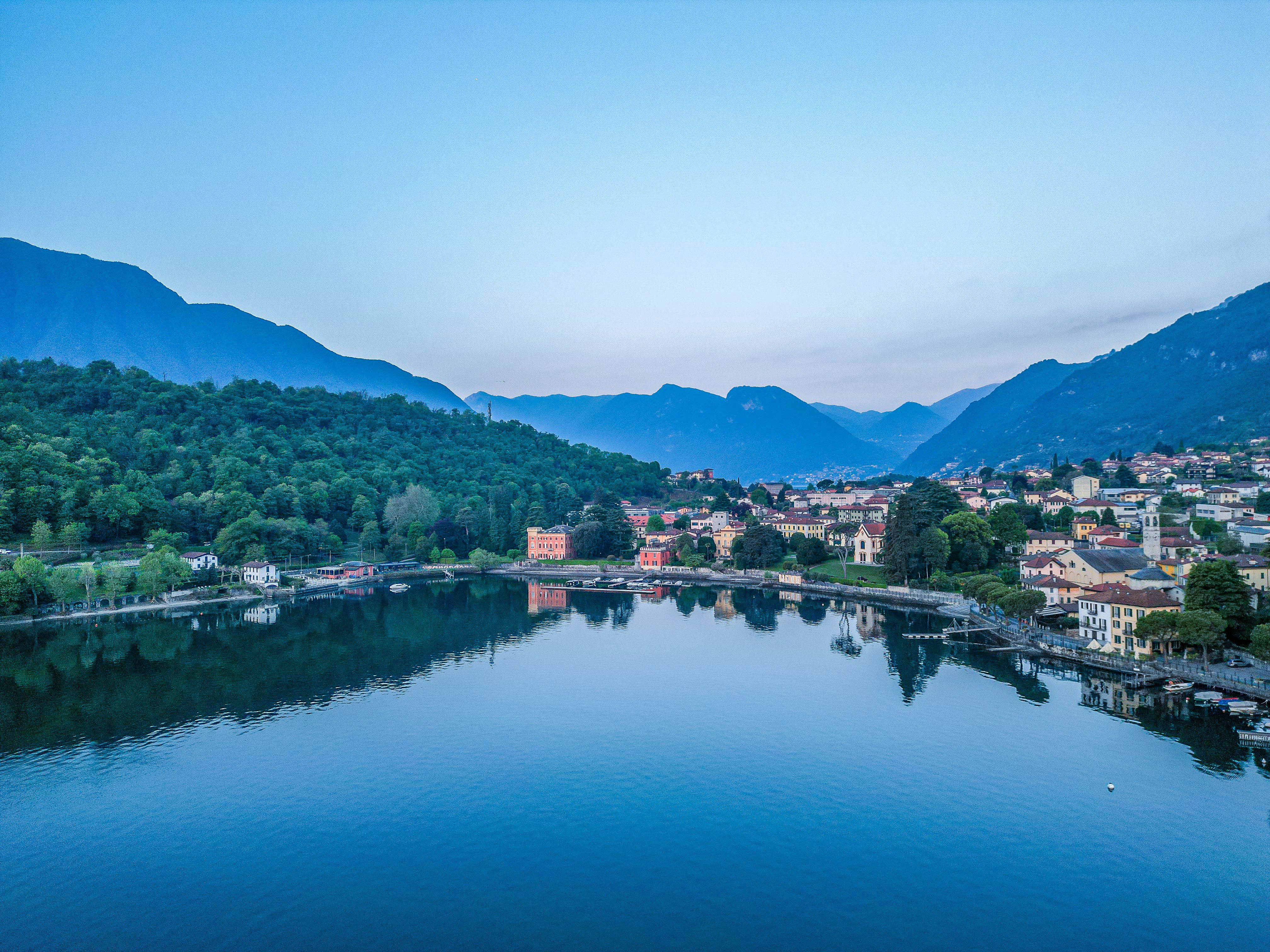 Calm lake reflects mountains and a town at dusk.