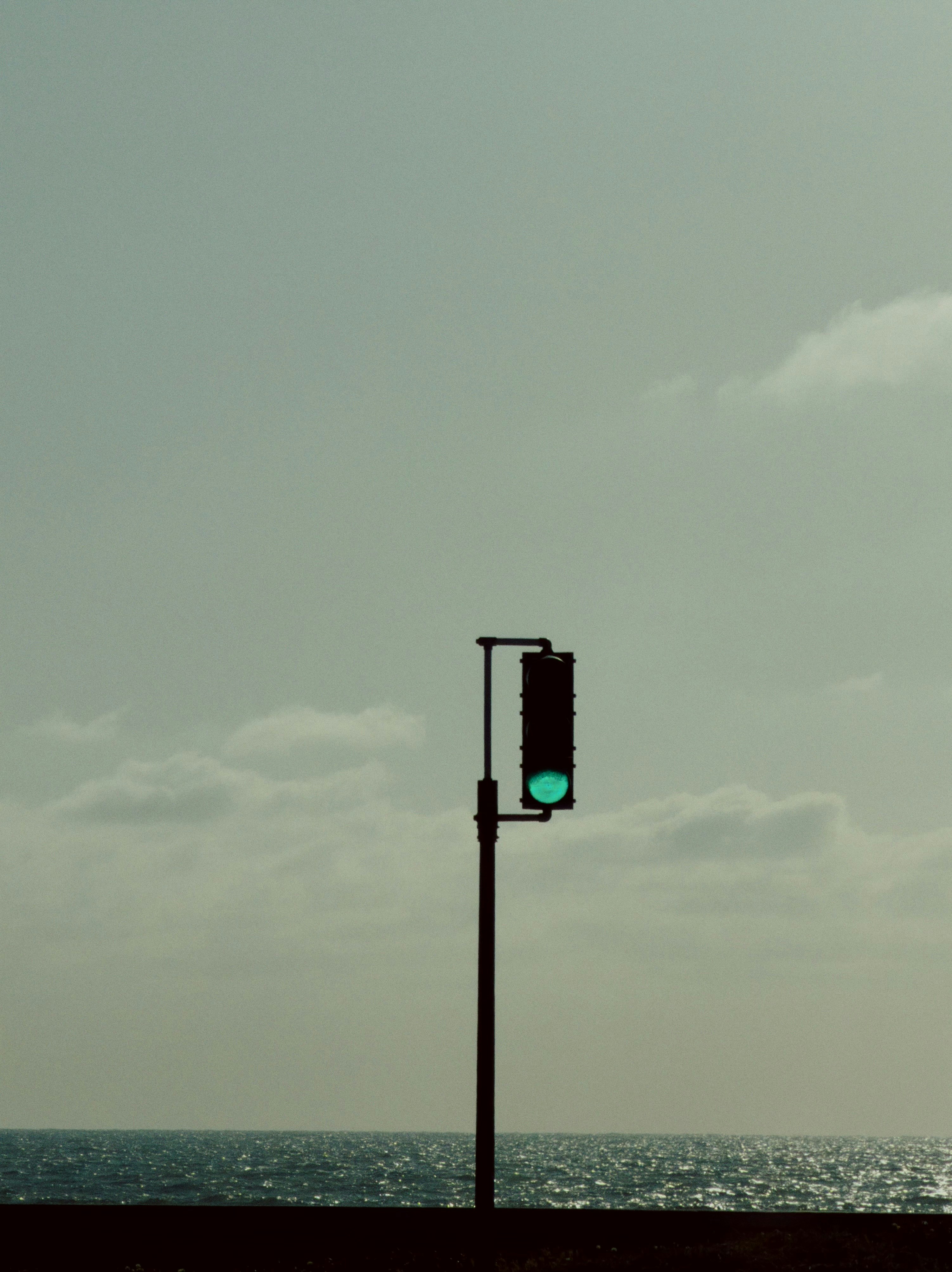 Traffic light with green signal against cloudy sky and ocean.