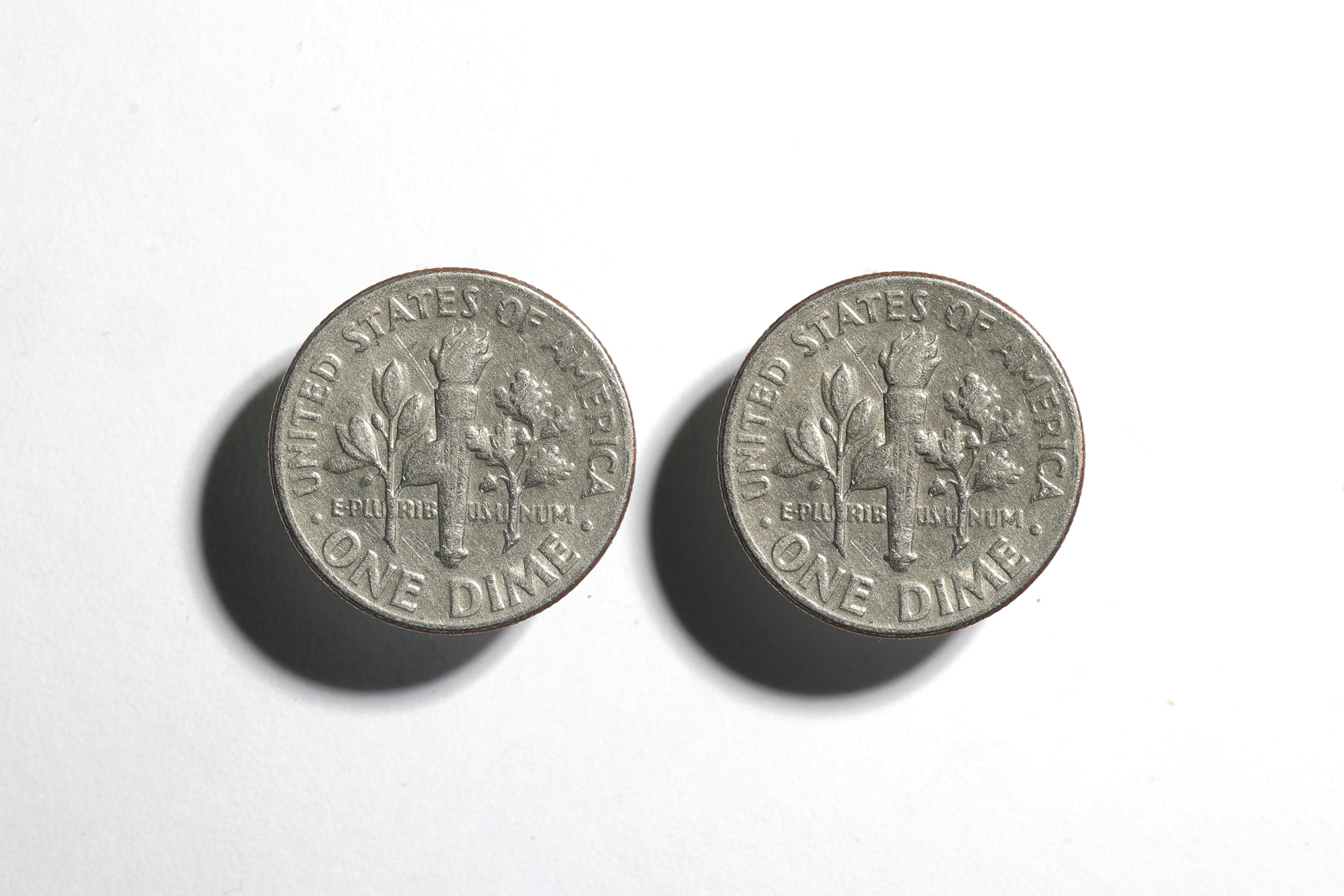 Two united states dimes on a white surface.