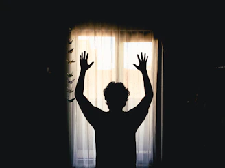 Silhouette of a person with arms raised at window