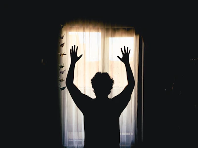 Silhouette of a person with arms raised at window