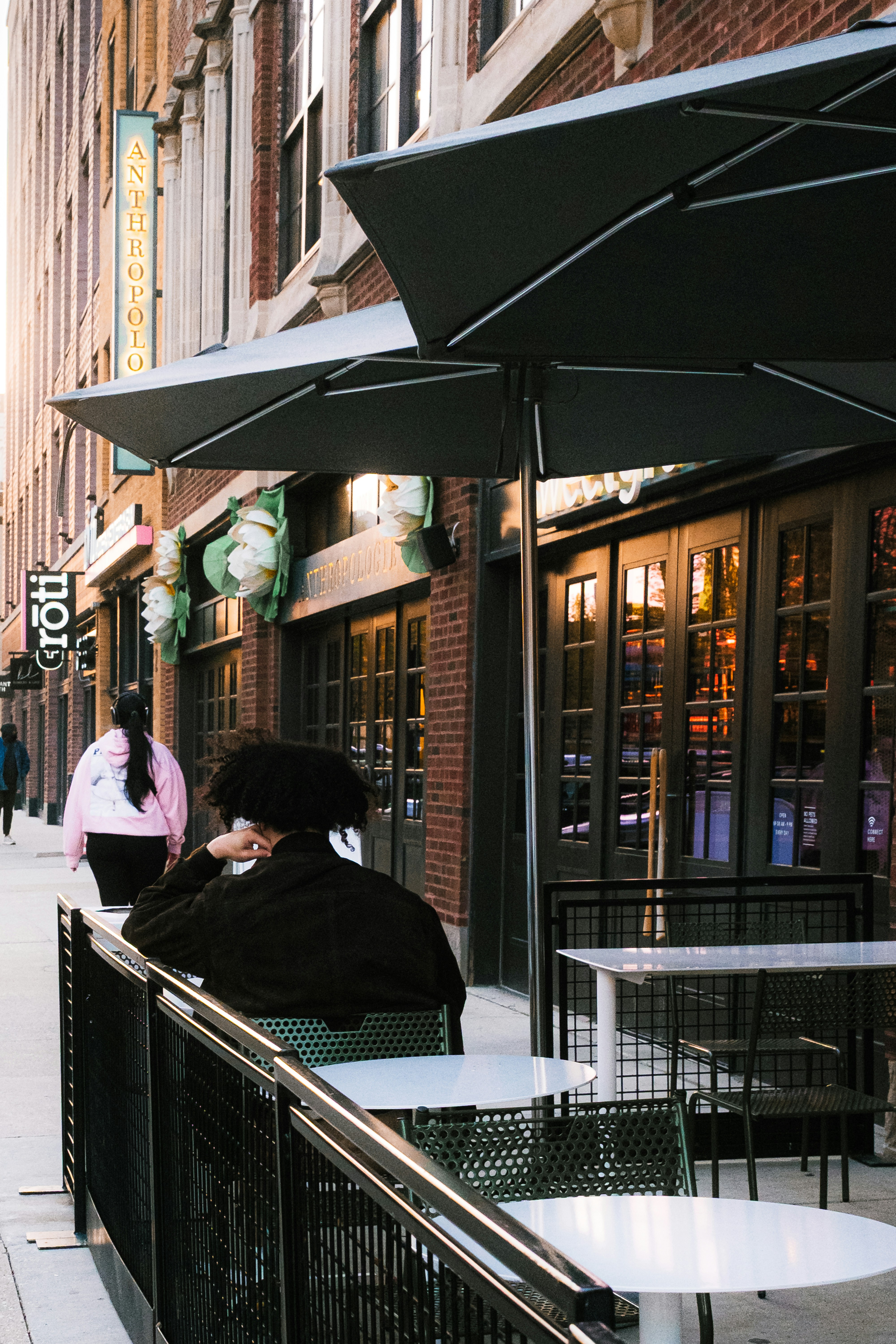 Person sitzt am Außentisch in einem Café in der Nähe eines Backsteingebäudes.