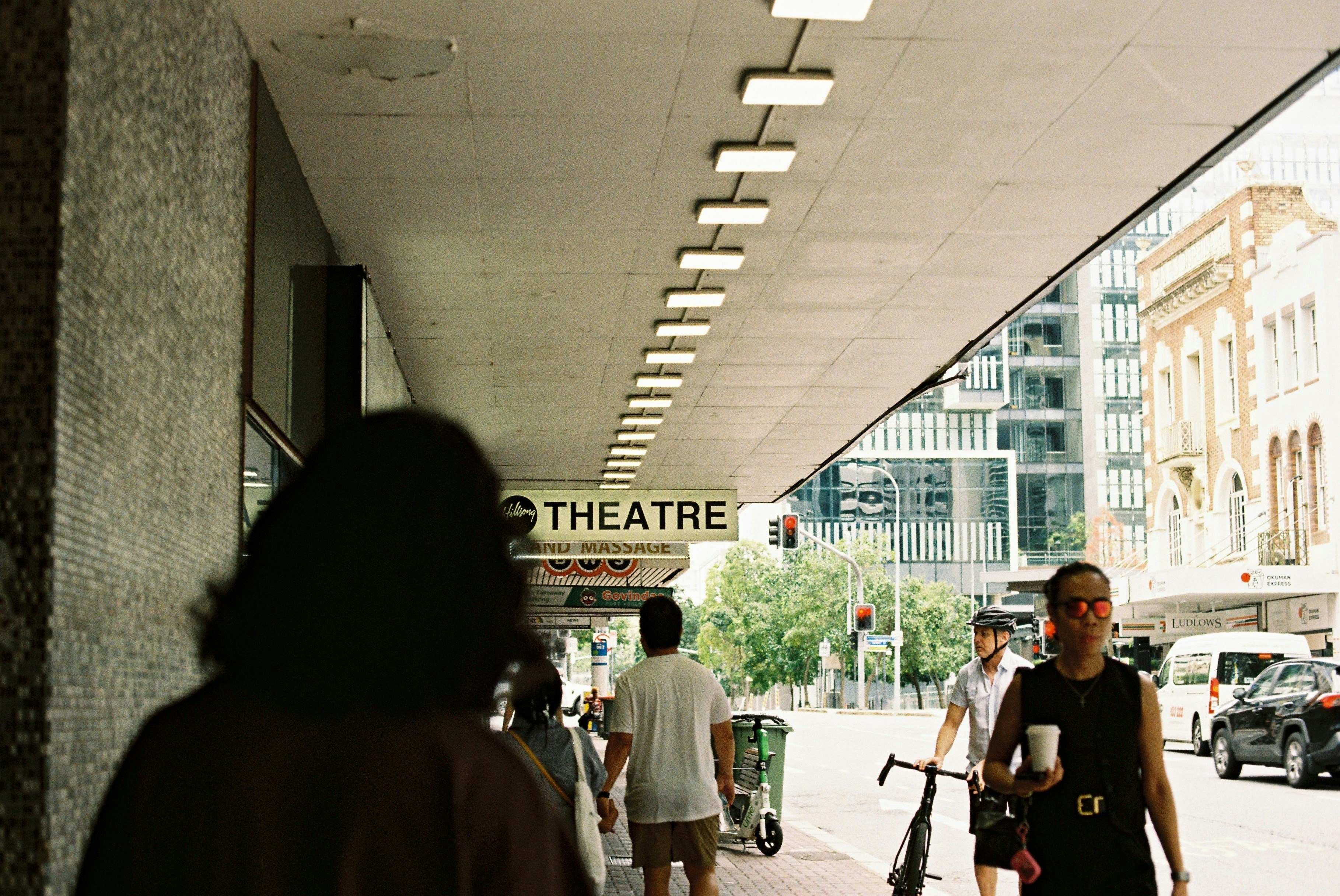 People walk along a city street under a theater sign.