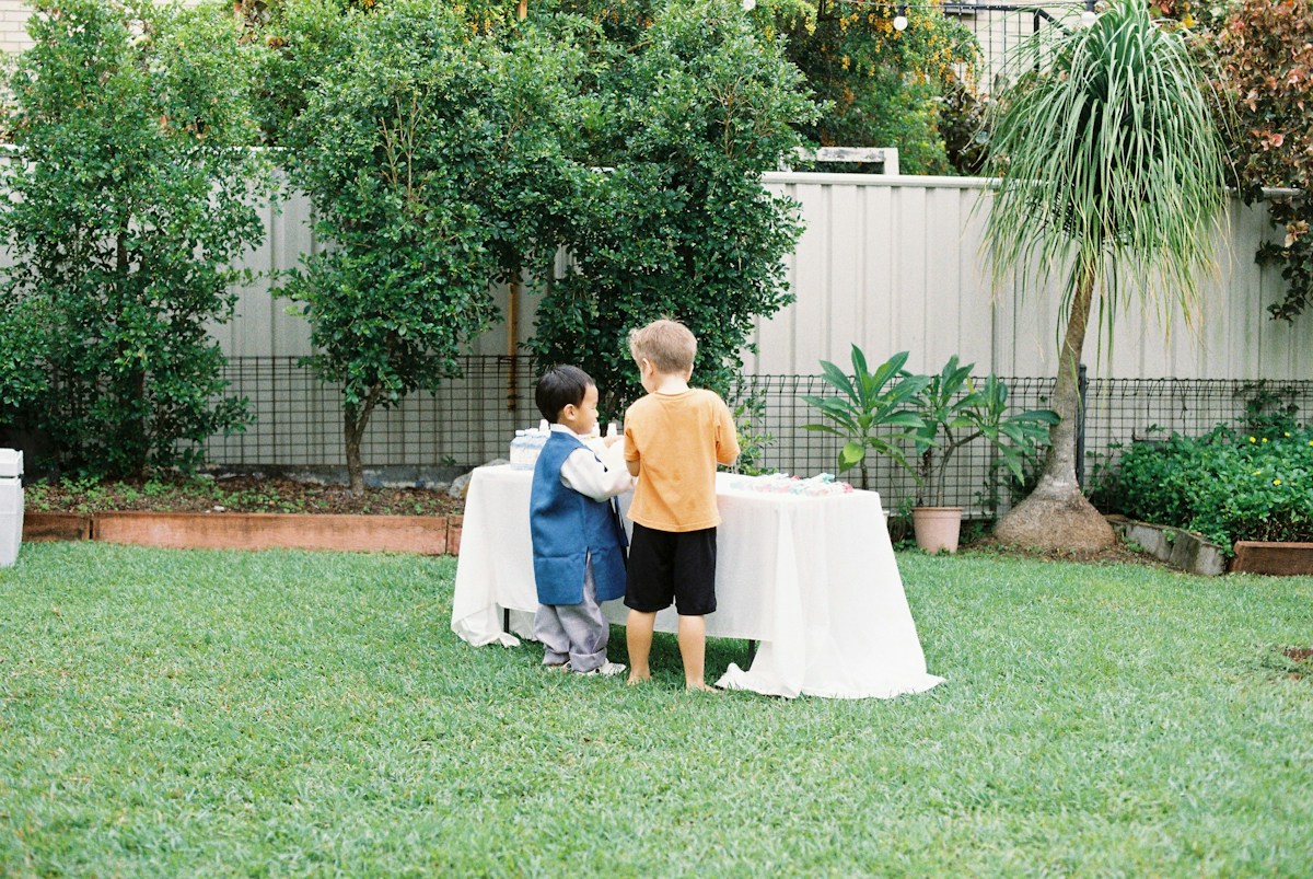 Two young children stand by a decorated table in a backyard, showcasing a 2026 graduation party theme.