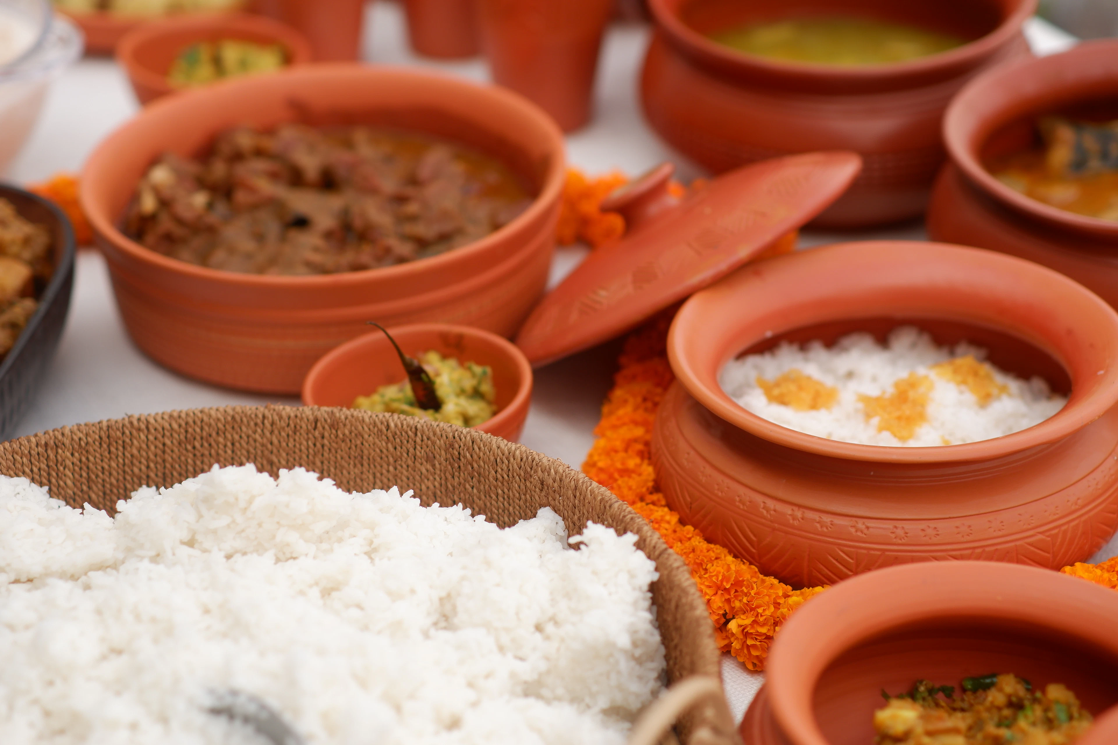 Indian mutton curry, dal, rice and rice pudding served in lidded terracotta pots at a festive spread laid out with marigold garlands