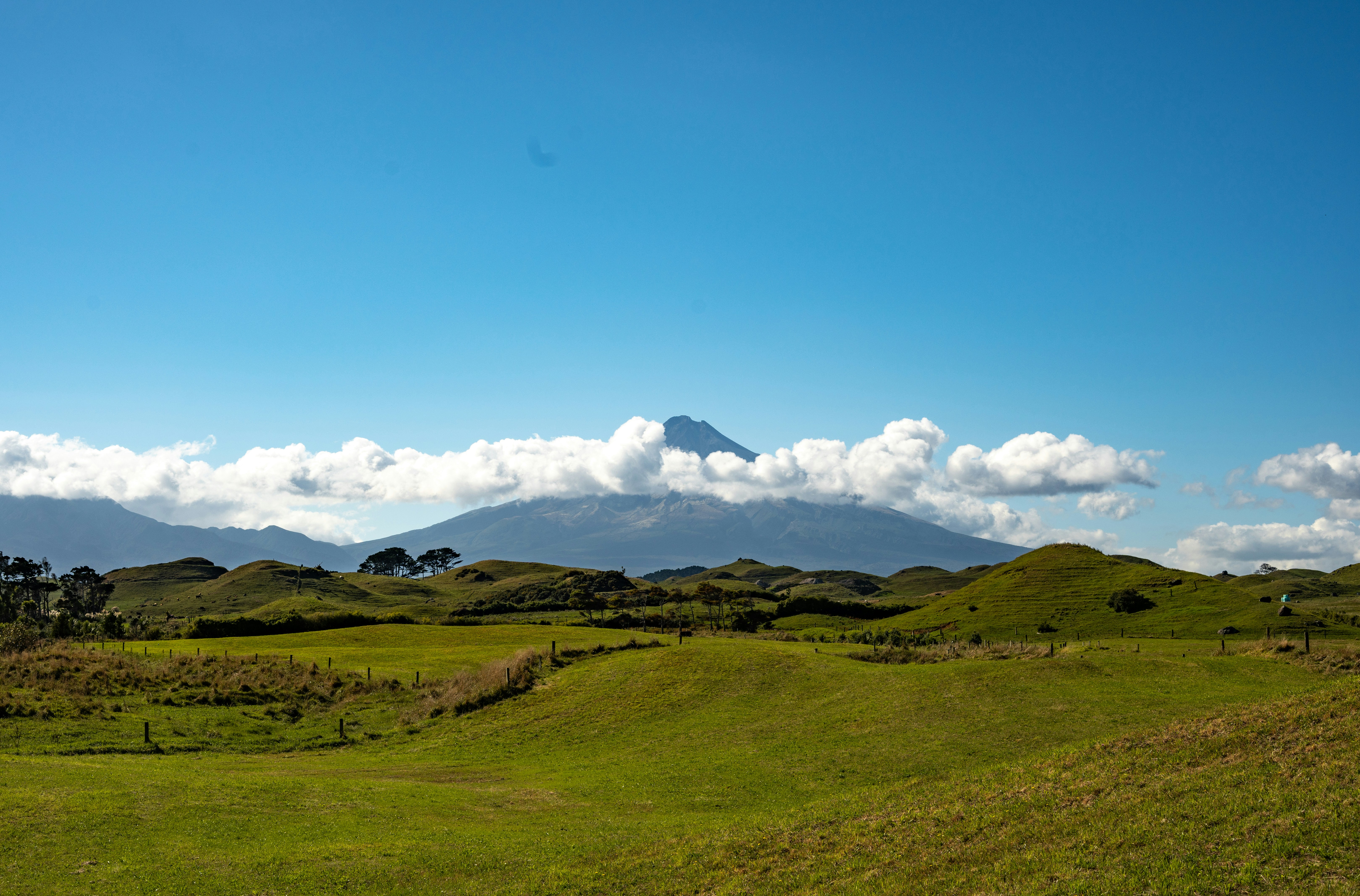Mountain peak emerges from clouds above rolling green hills.