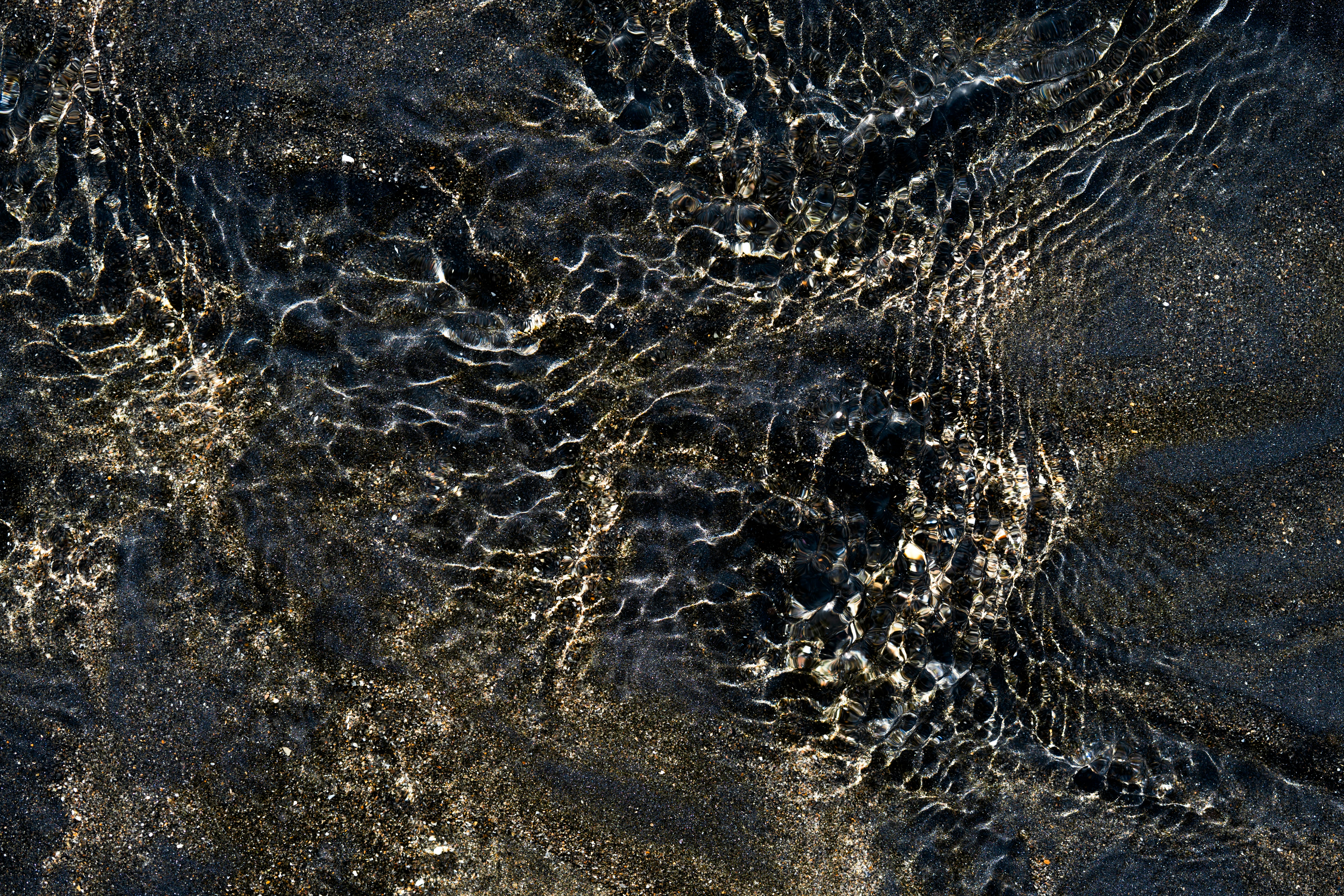 El agua ondulando sobre arena oscura crea patrones abstractos