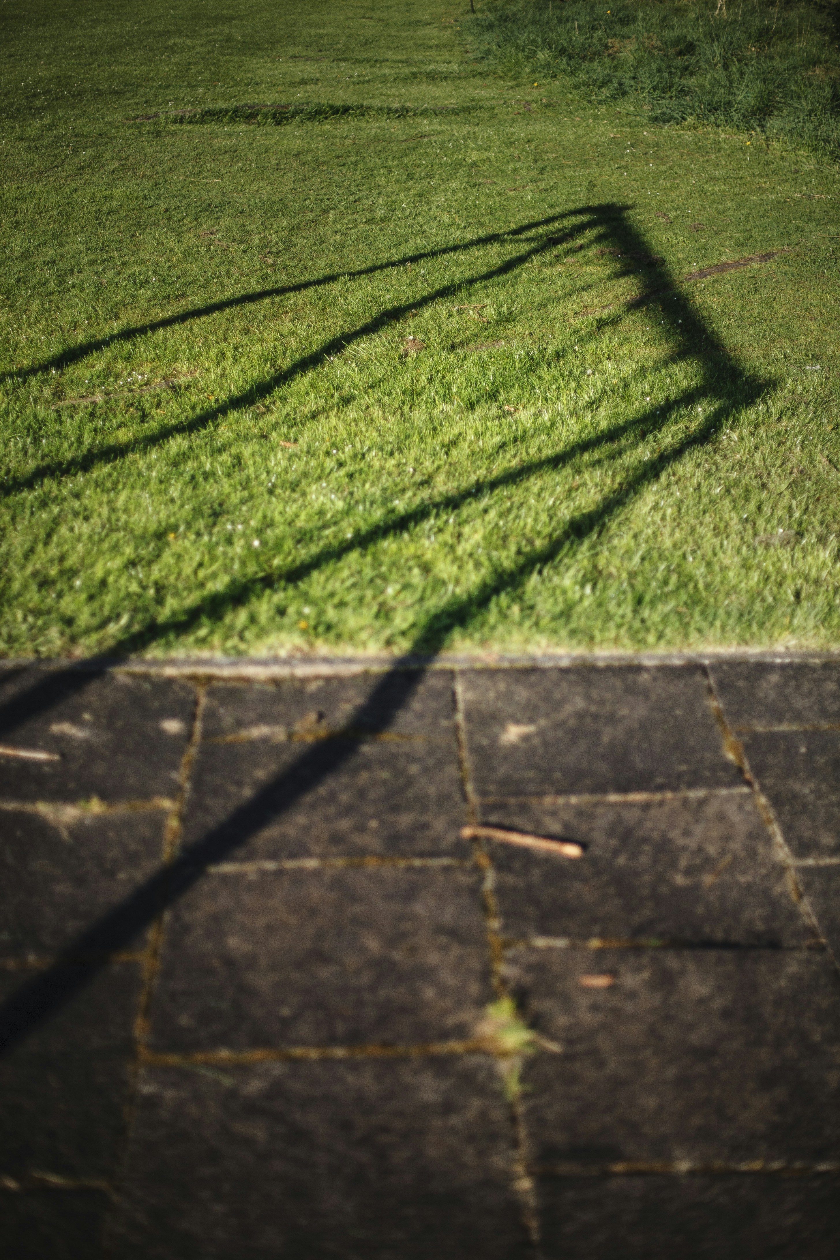 Sombras de uma estrutura na grama e no asfalto.