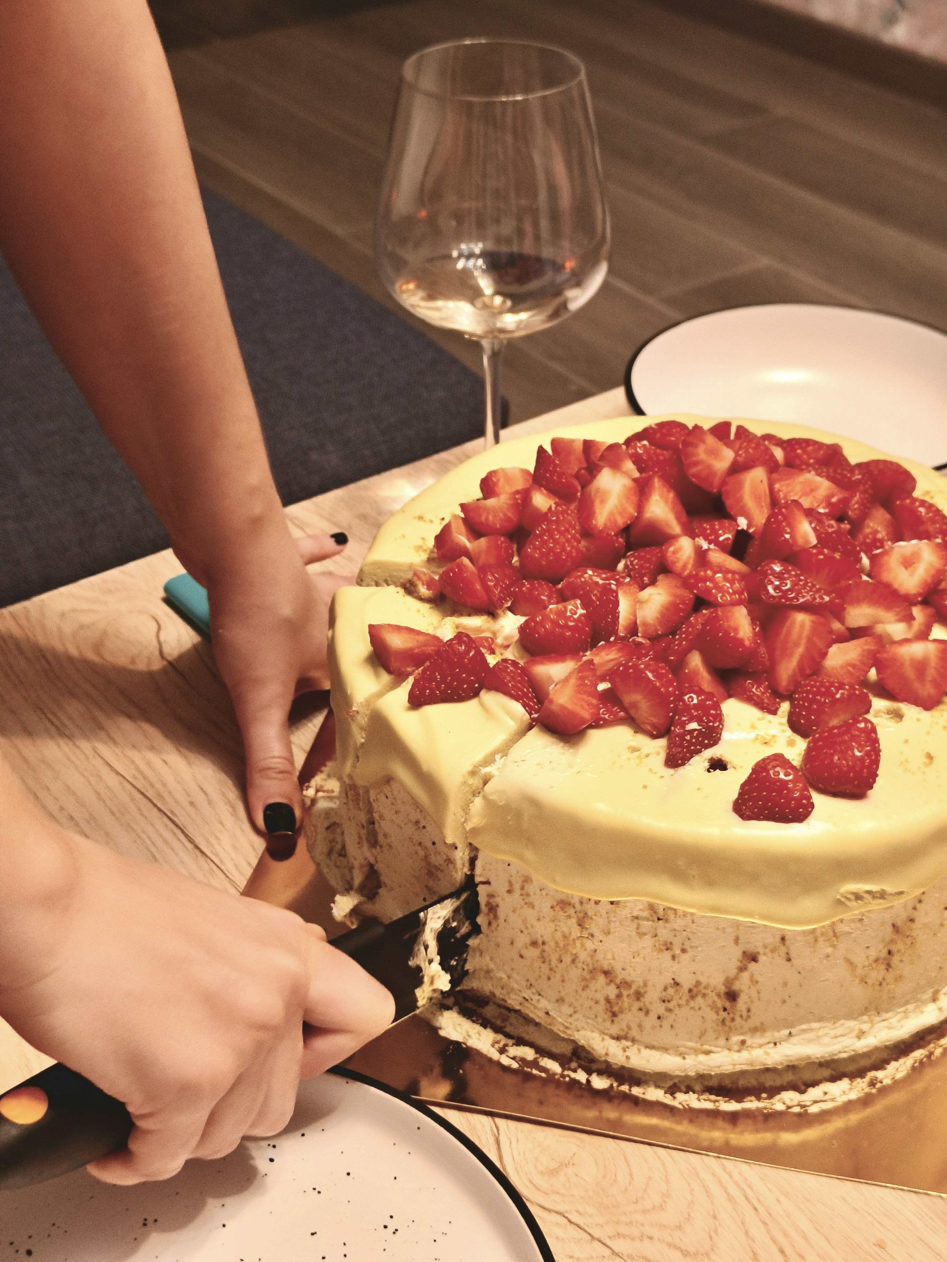 Cutting a strawberry cake with a glass of wine.